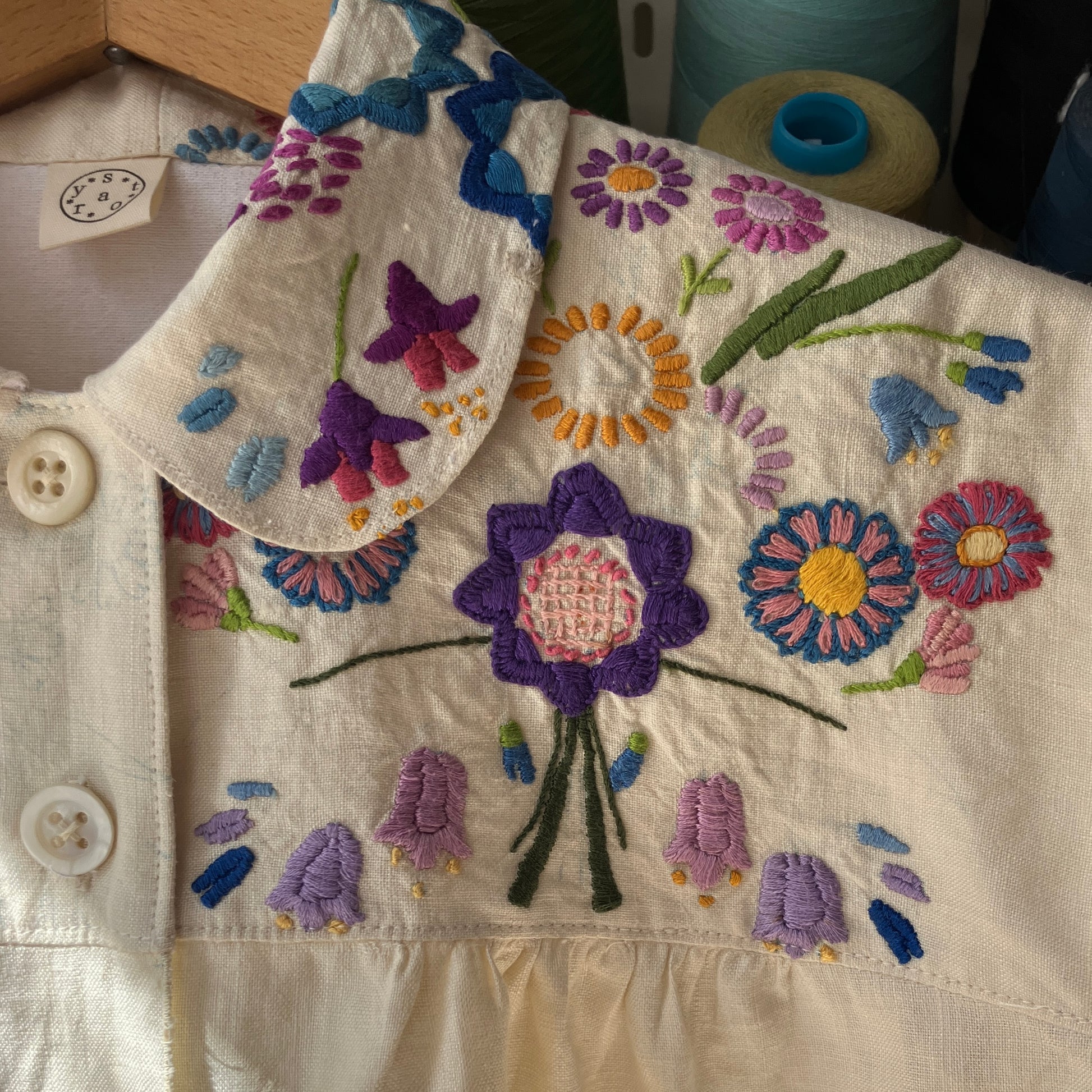 Shirt made from a recycled off-white linen tablecloth with embroidered floral design in various stages of completion