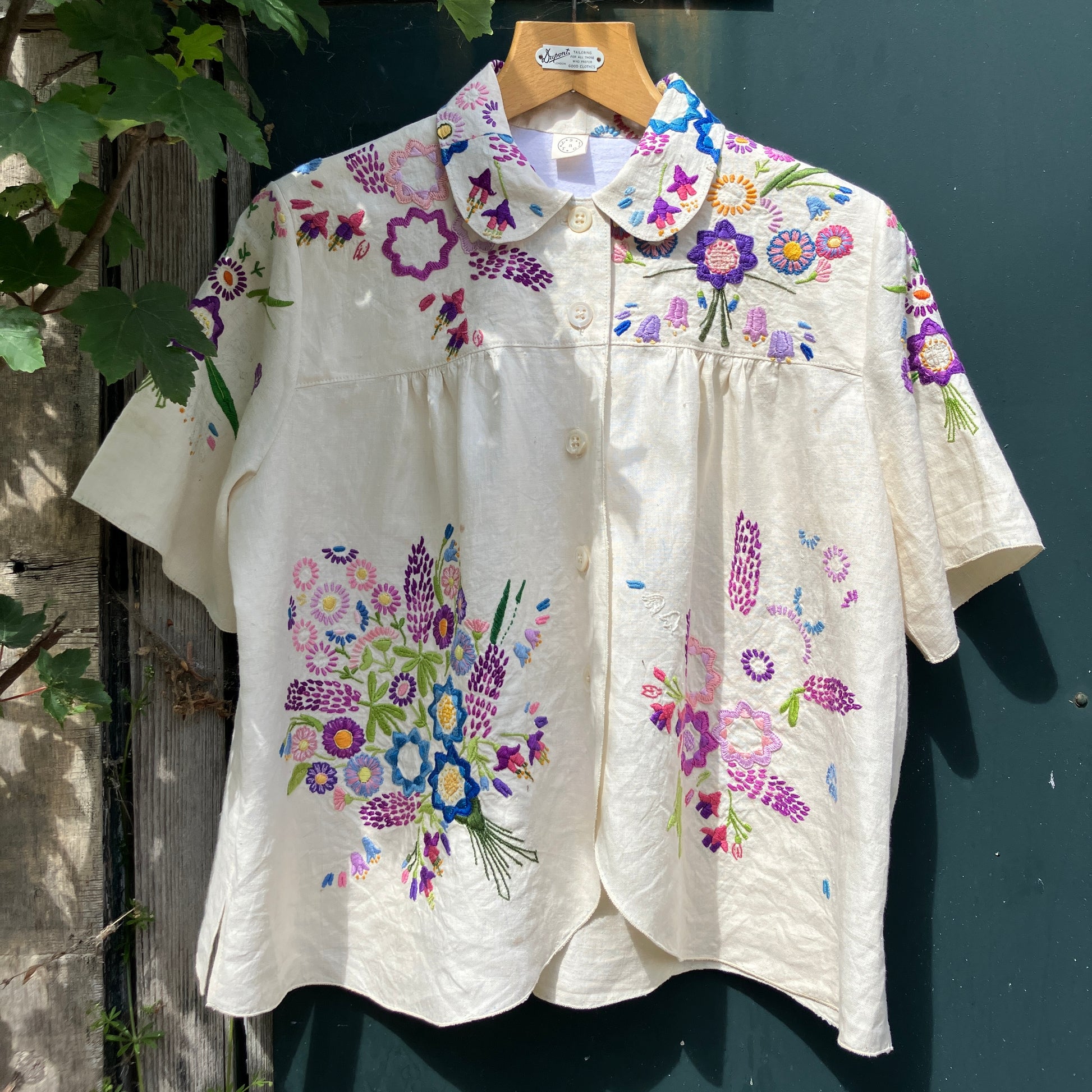 Shirt made from a recycled off-white linen tablecloth with embroidered floral design in various stages of completion