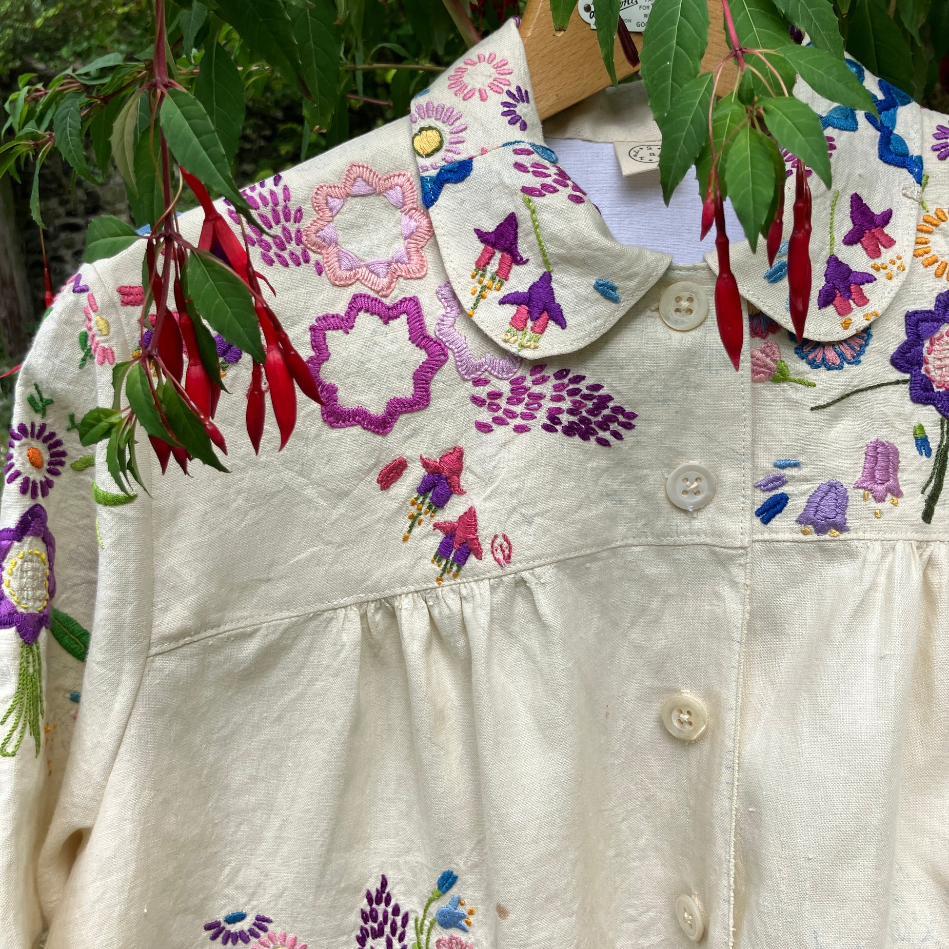 Shirt made from a recycled off-white linen tablecloth with embroidered floral design in various stages of completion