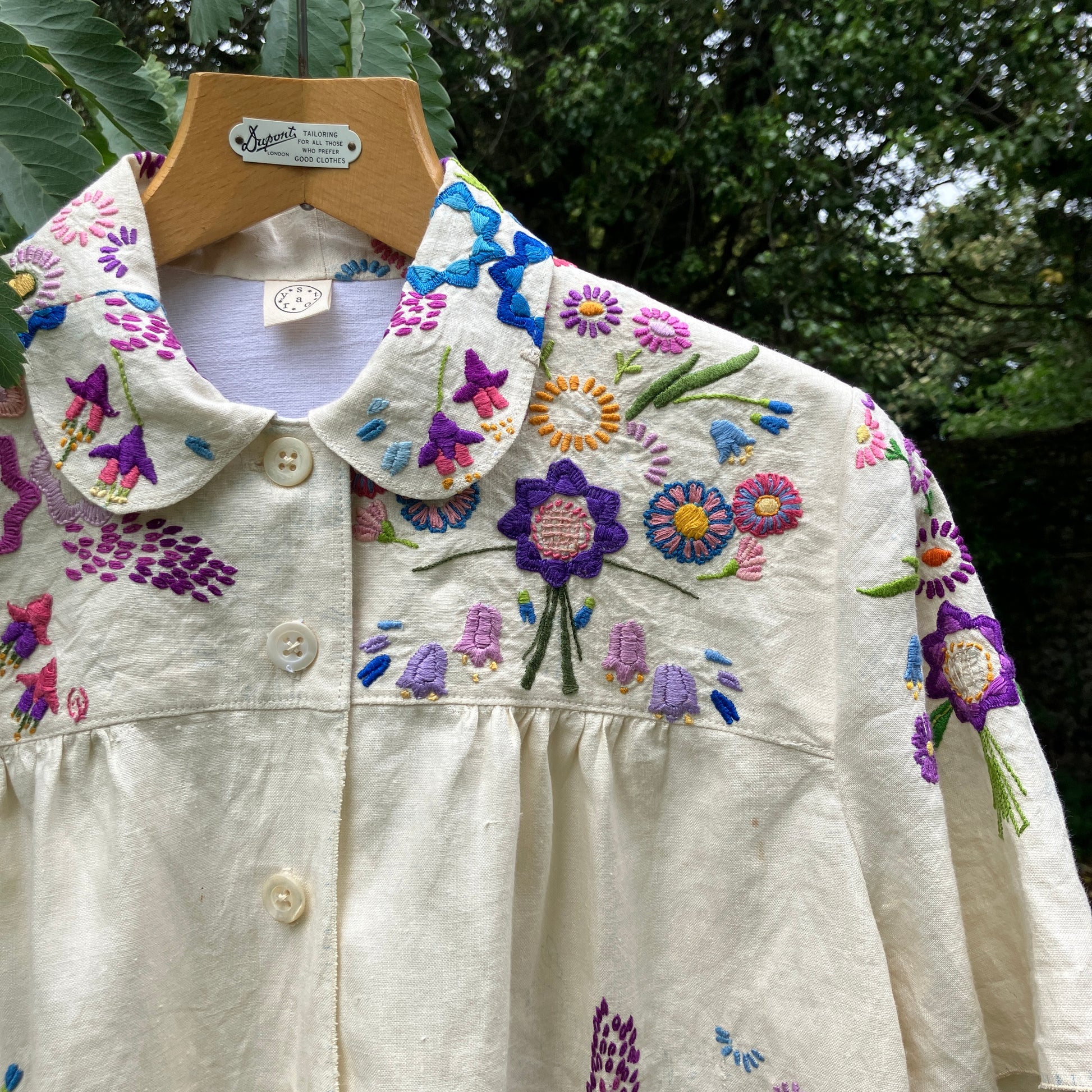 Shirt made from a recycled off-white linen tablecloth with embroidered floral design in various stages of completion