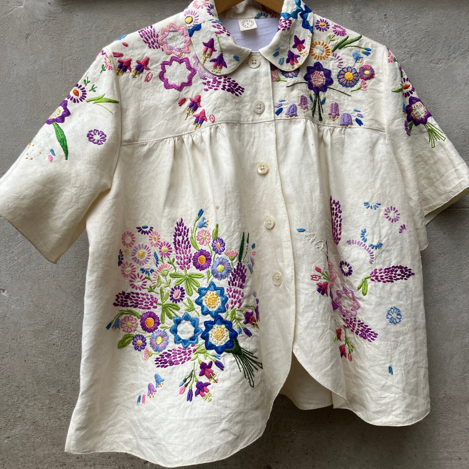 Shirt made from a recycled off-white linen tablecloth with embroidered floral design in various stages of completion