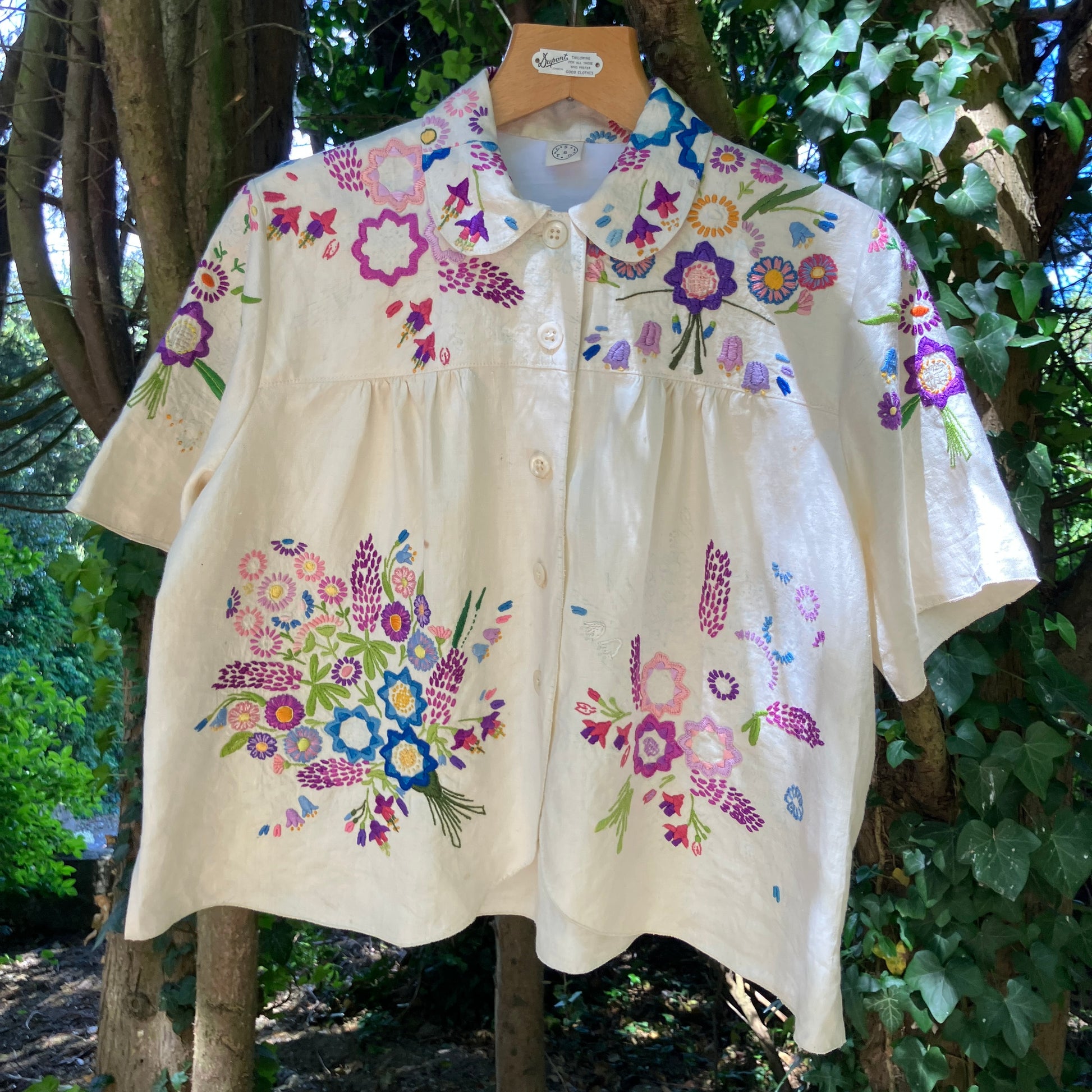 Shirt made from a recycled off-white linen tablecloth with embroidered floral design in various stages of completion