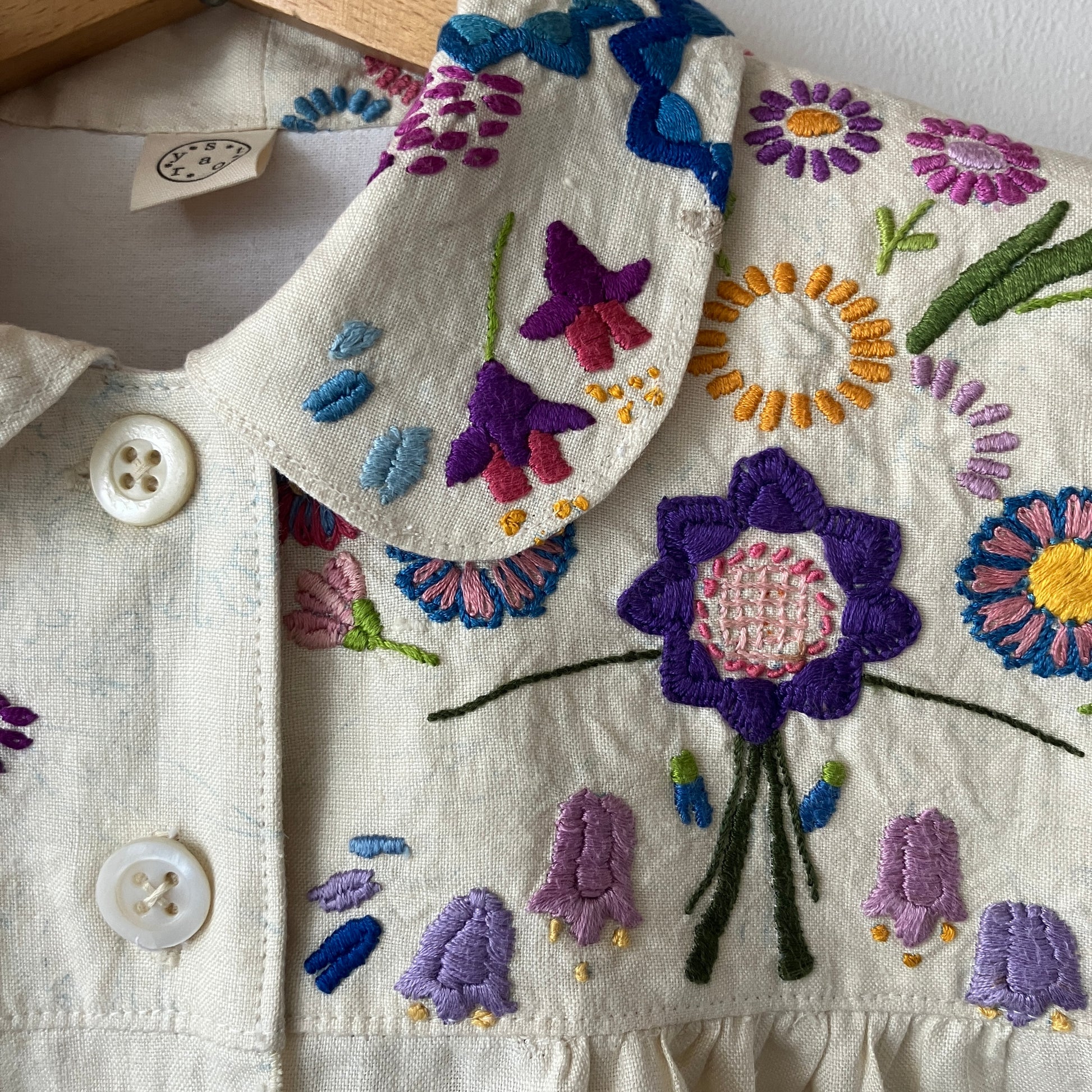 Shirt made from a recycled off-white linen tablecloth with embroidered floral design in various stages of completion