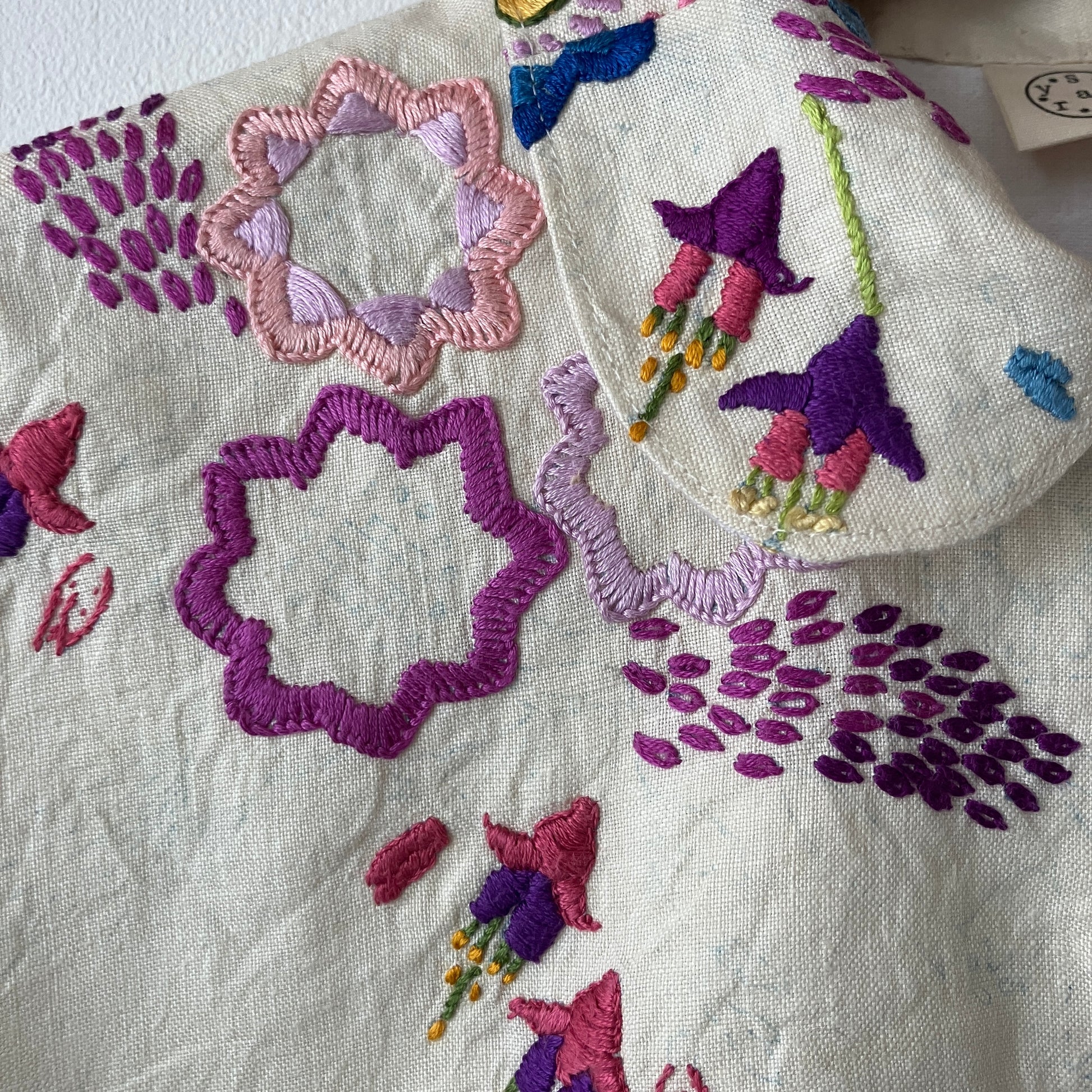Shirt made from a recycled off-white linen tablecloth with embroidered floral design in various stages of completion