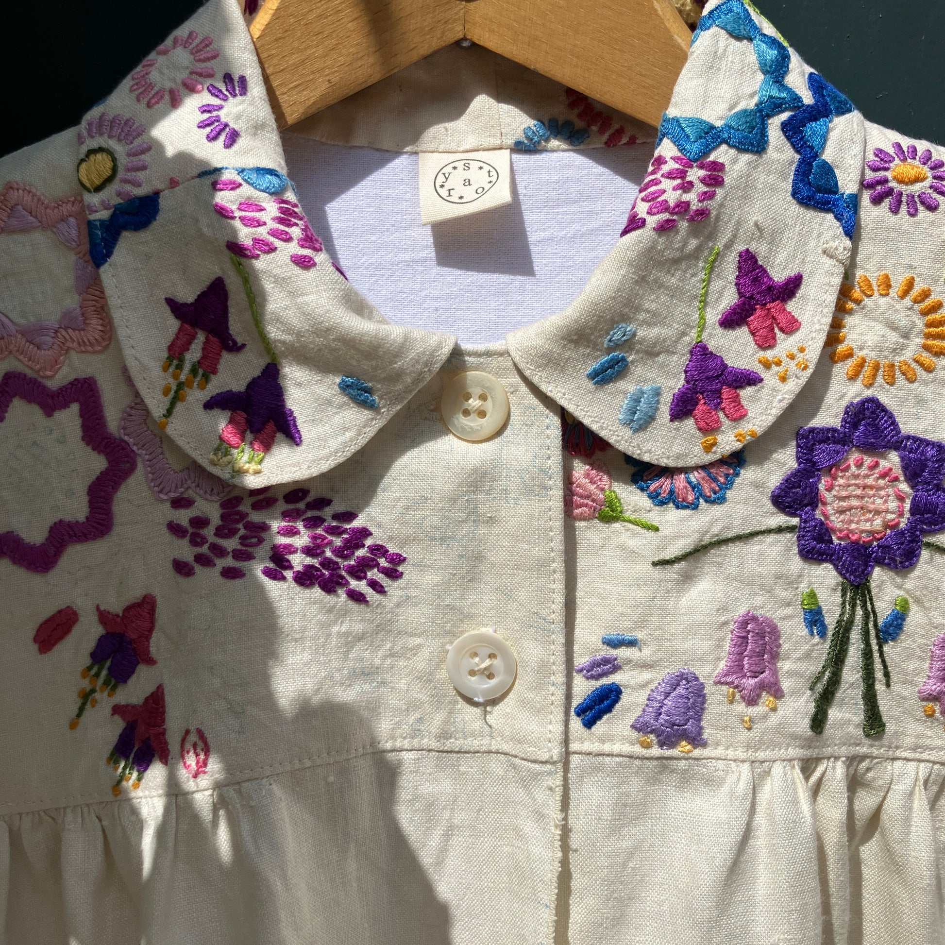 Shirt made from a recycled off-white linen tablecloth with embroidered floral design in various stages of completion