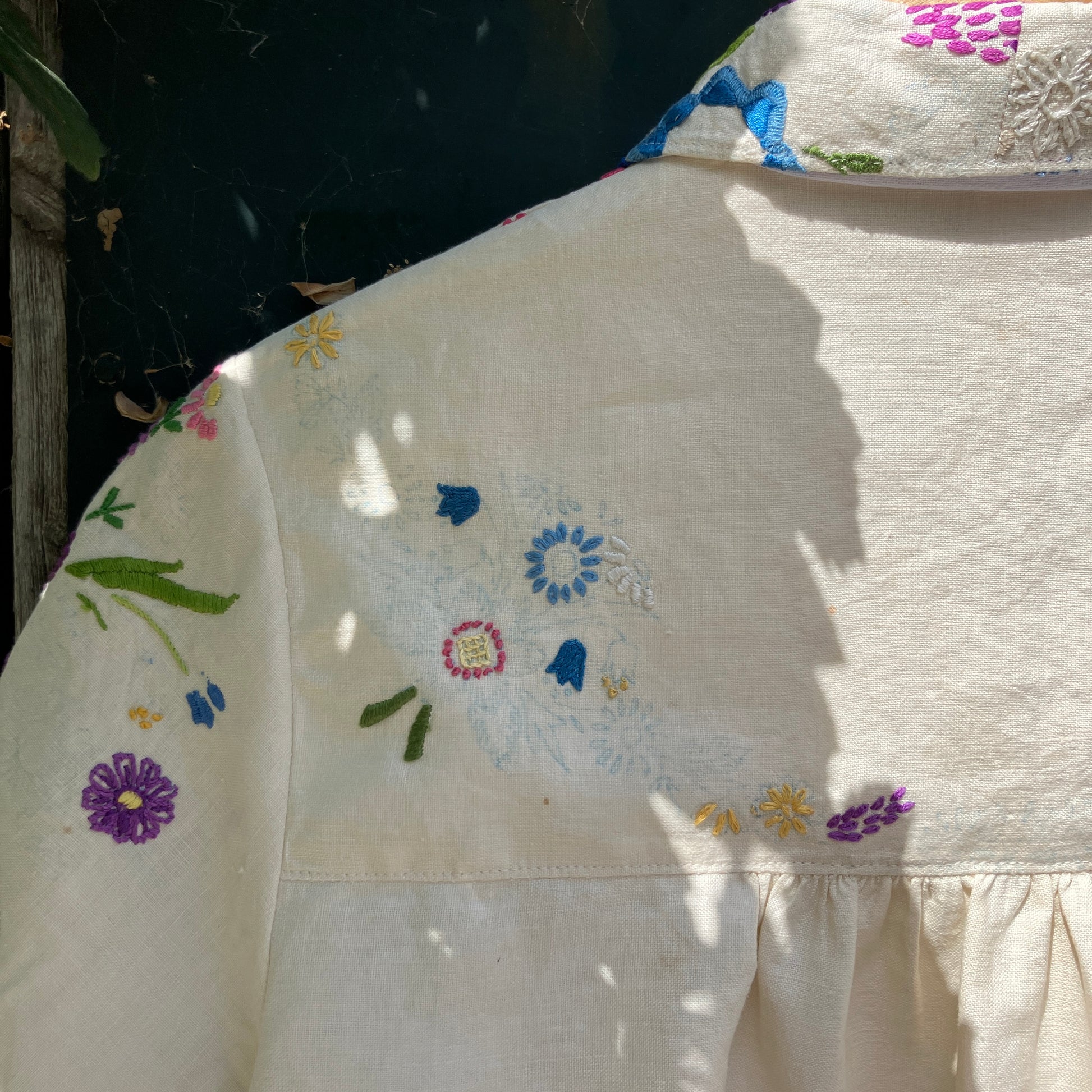 Shirt made from a recycled off-white linen tablecloth with embroidered floral design in various stages of completion