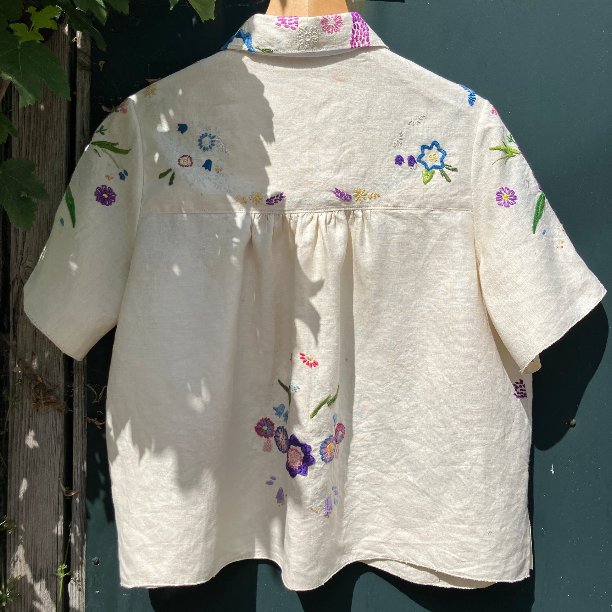 Shirt made from a recycled off-white linen tablecloth with embroidered floral design in various stages of completion
