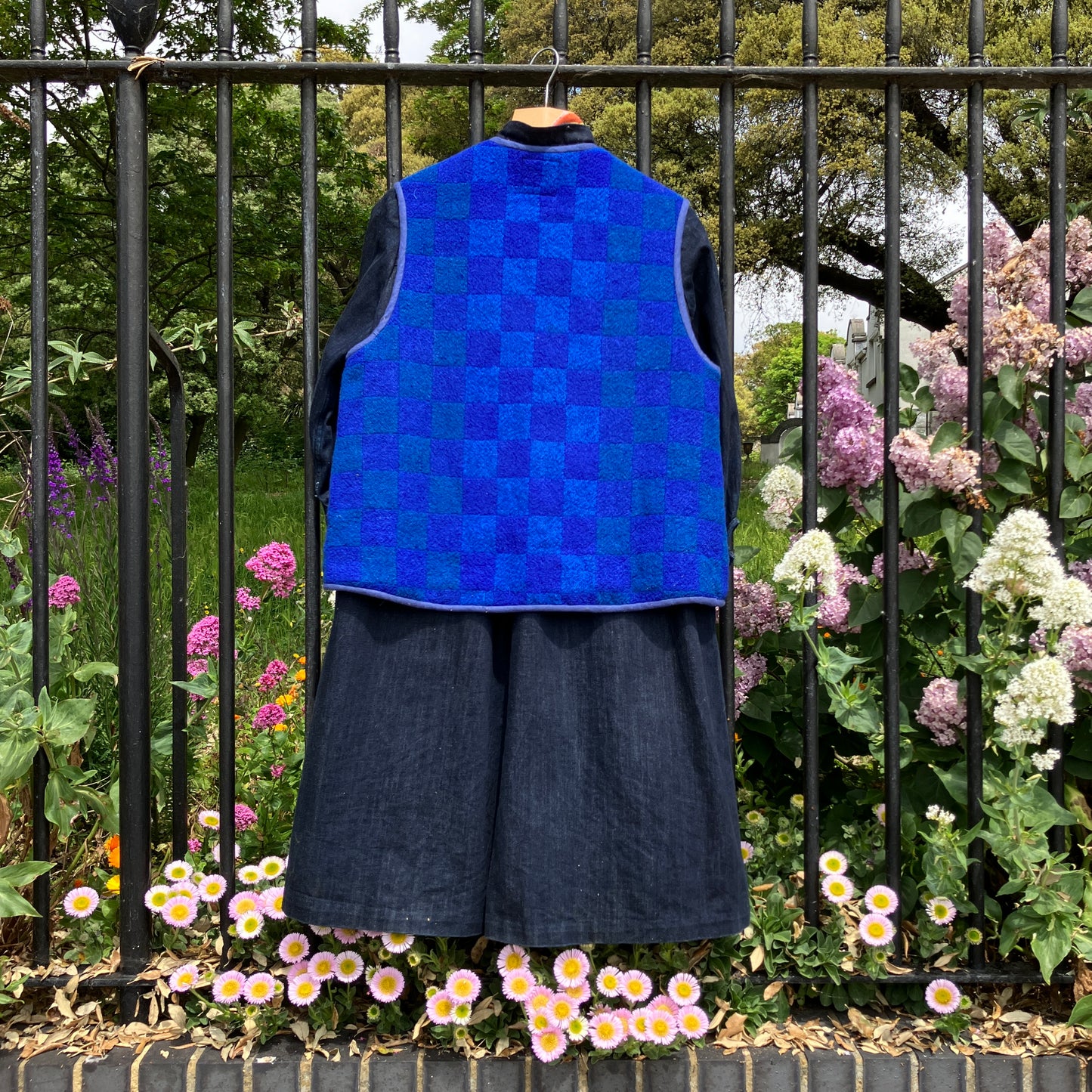 Vest/gilet/waistcoat made from a reclaimed blue checkerboard weave Irish wool Gaiety blanket, photographed in front of a lilac bush (back view)