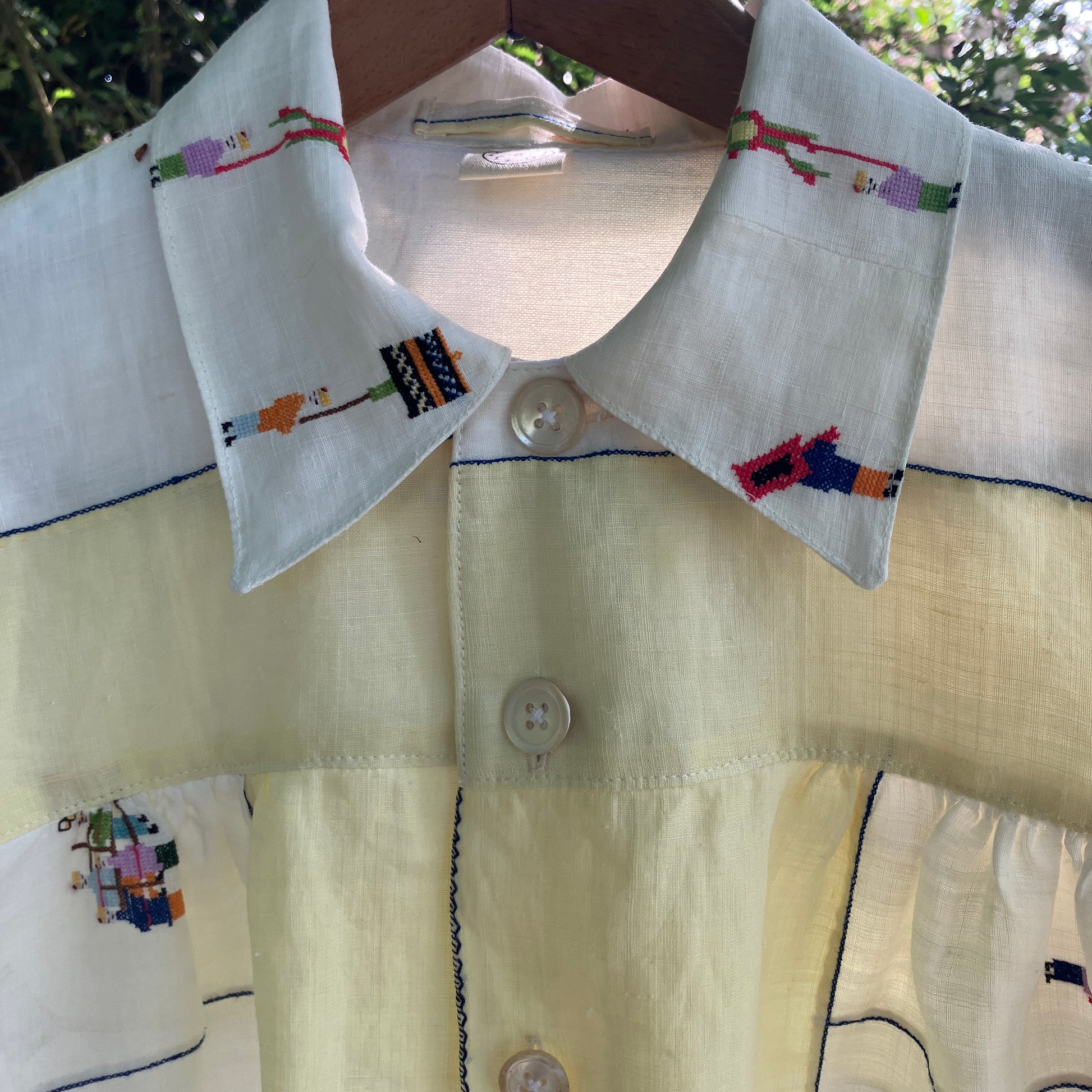 Shirt made from a found vintage tablecloth with a parade of small embroidered figures holding signs, kites and lanterns