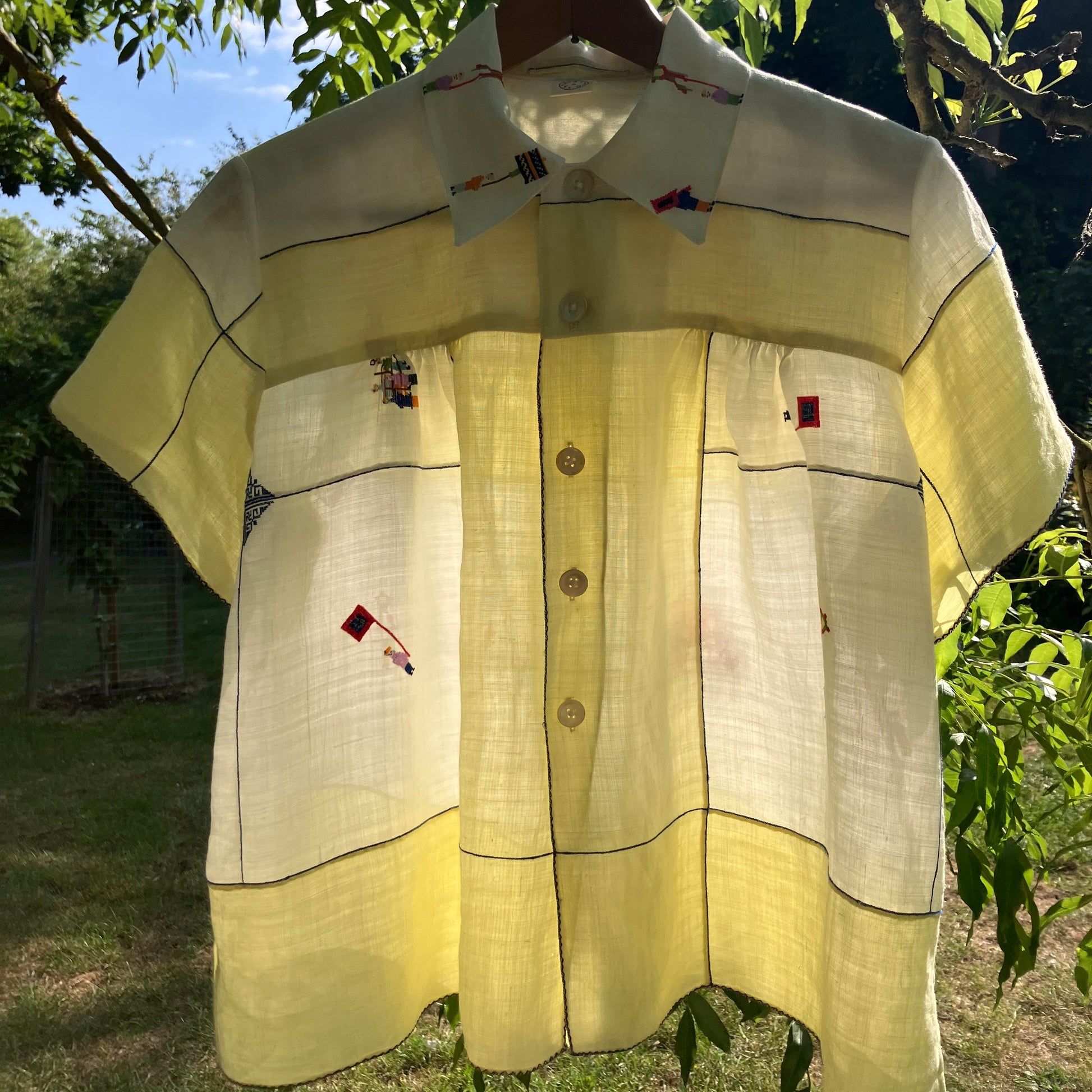 Shirt made from a found vintage tablecloth with a parade of small embroidered figures holding signs, kites and lanterns