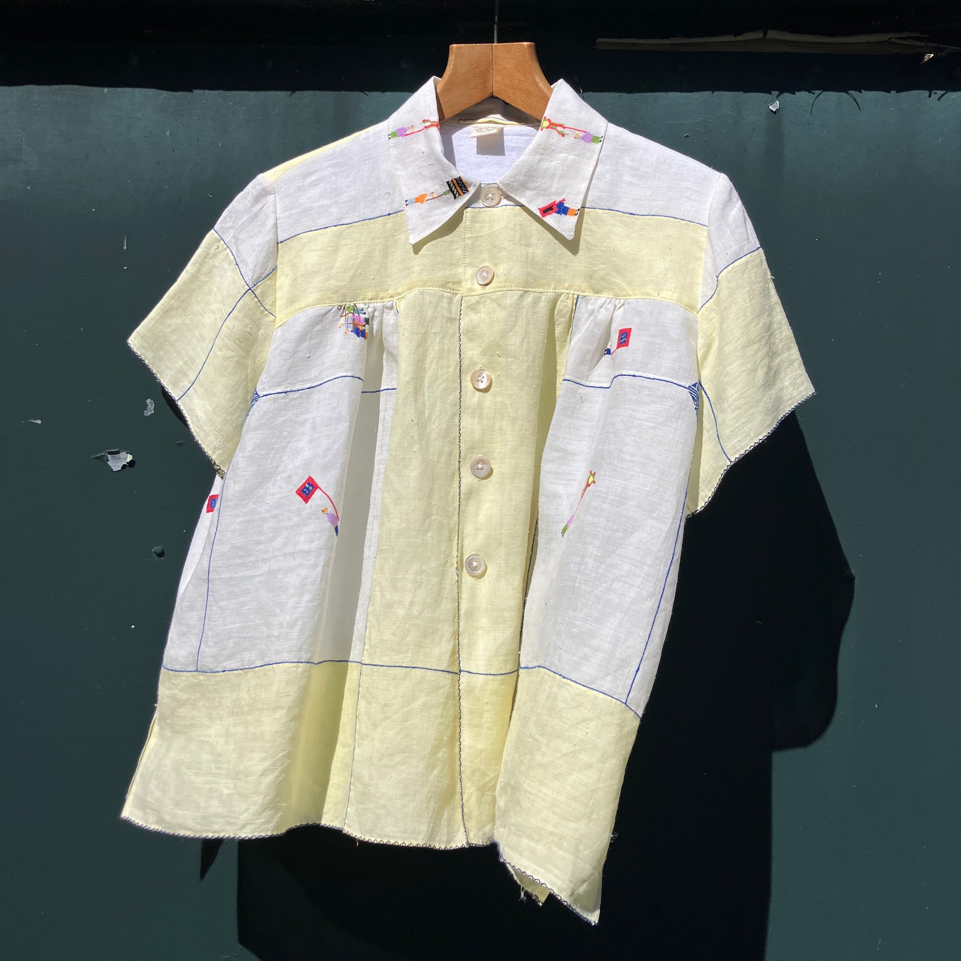 Shirt made from a found vintage tablecloth with a parade of small embroidered figures holding signs, kites and lanterns