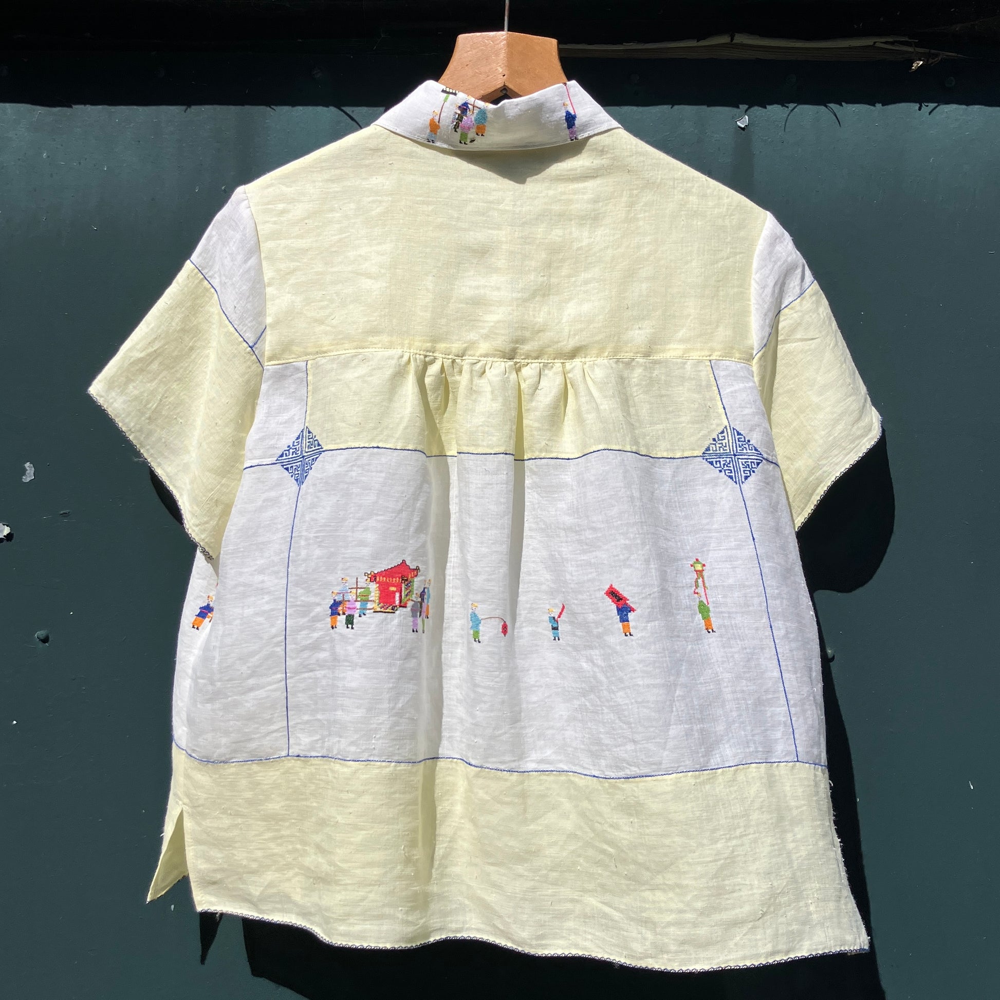 Shirt made from a found vintage tablecloth with a parade of small embroidered figures holding signs, kites and lanterns
