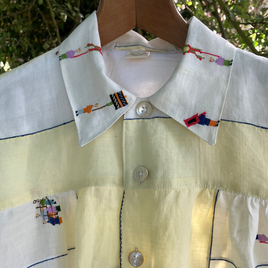 Shirt made from a found vintage tablecloth with a parade of small embroidered figures holding signs, kites and lanterns