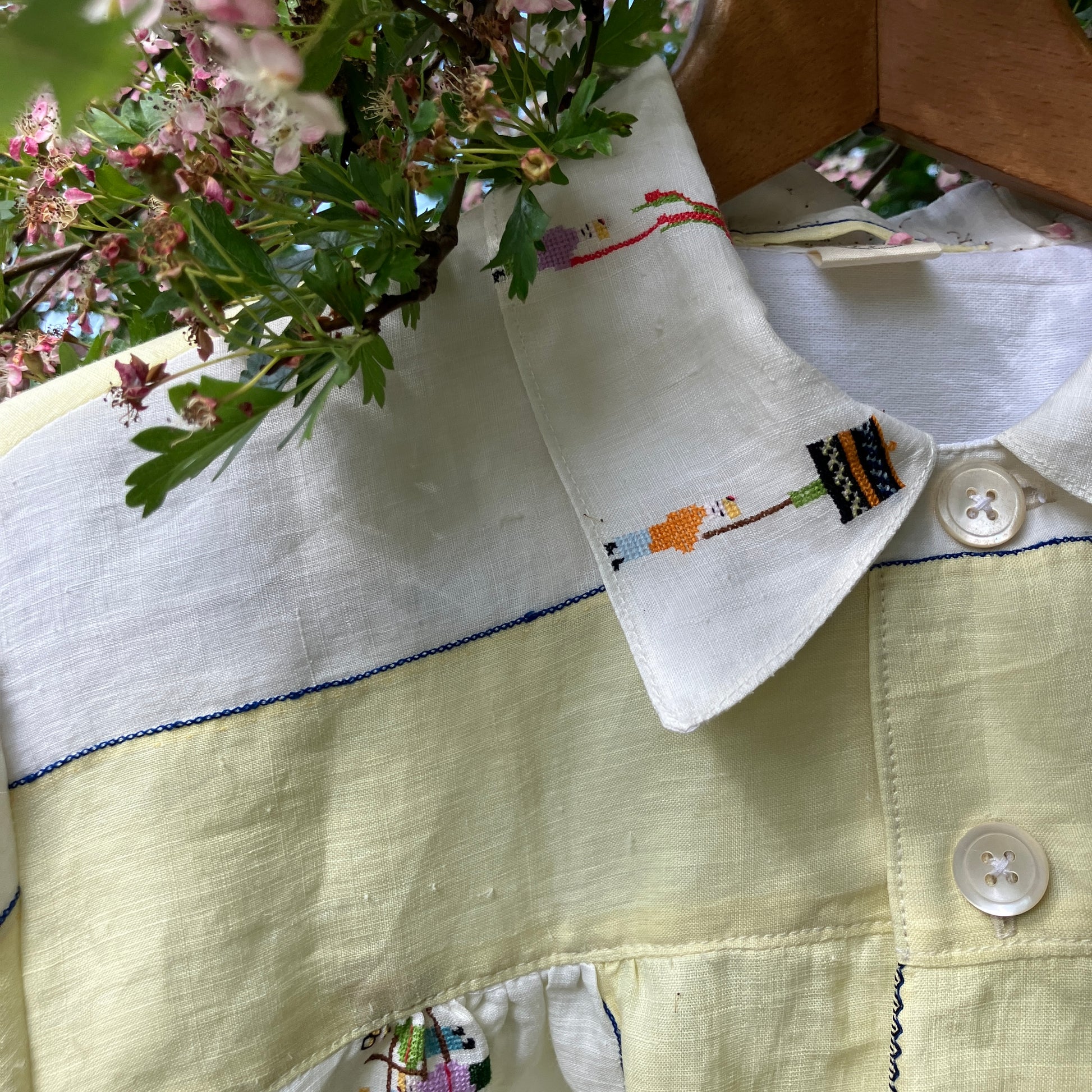 Shirt made from a found vintage tablecloth with a parade of small embroidered figures holding signs, kites and lanterns