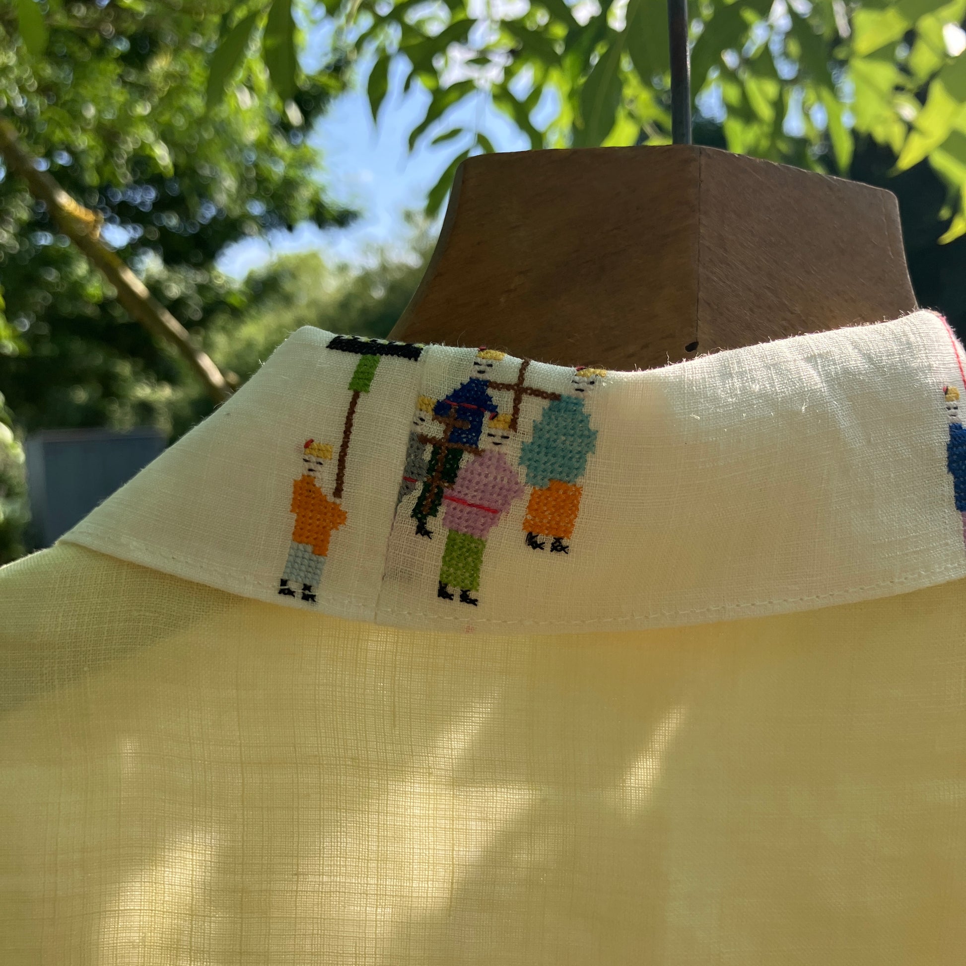 Shirt made from a found vintage tablecloth with a parade of small embroidered figures holding signs, kites and lanterns