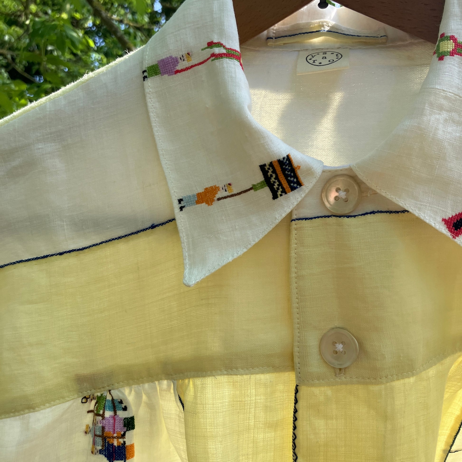 Shirt made from a found vintage tablecloth with a parade of small embroidered figures holding signs, kites and lanterns