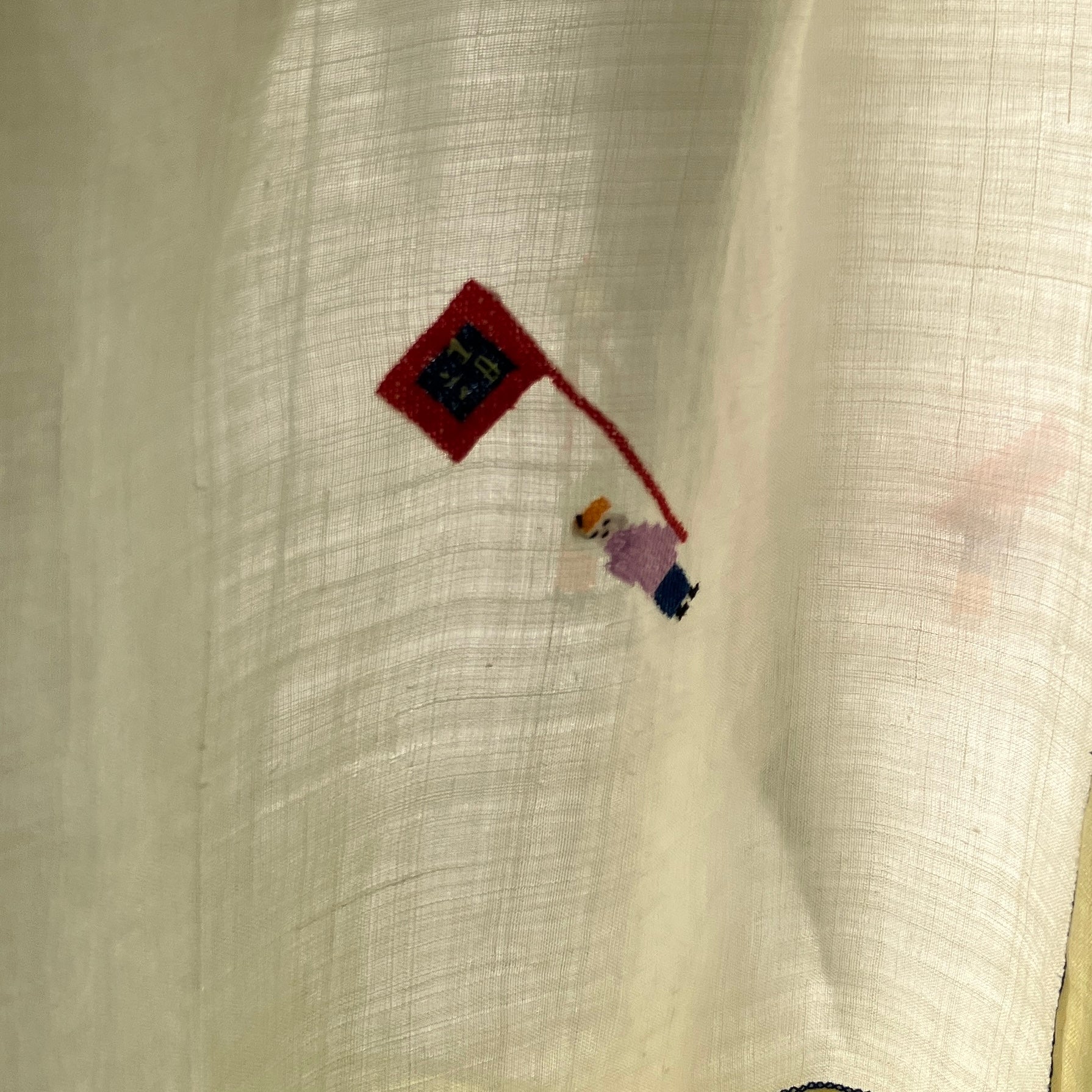 Shirt made from a found vintage tablecloth with a parade of small embroidered figures holding signs, kites and lanterns