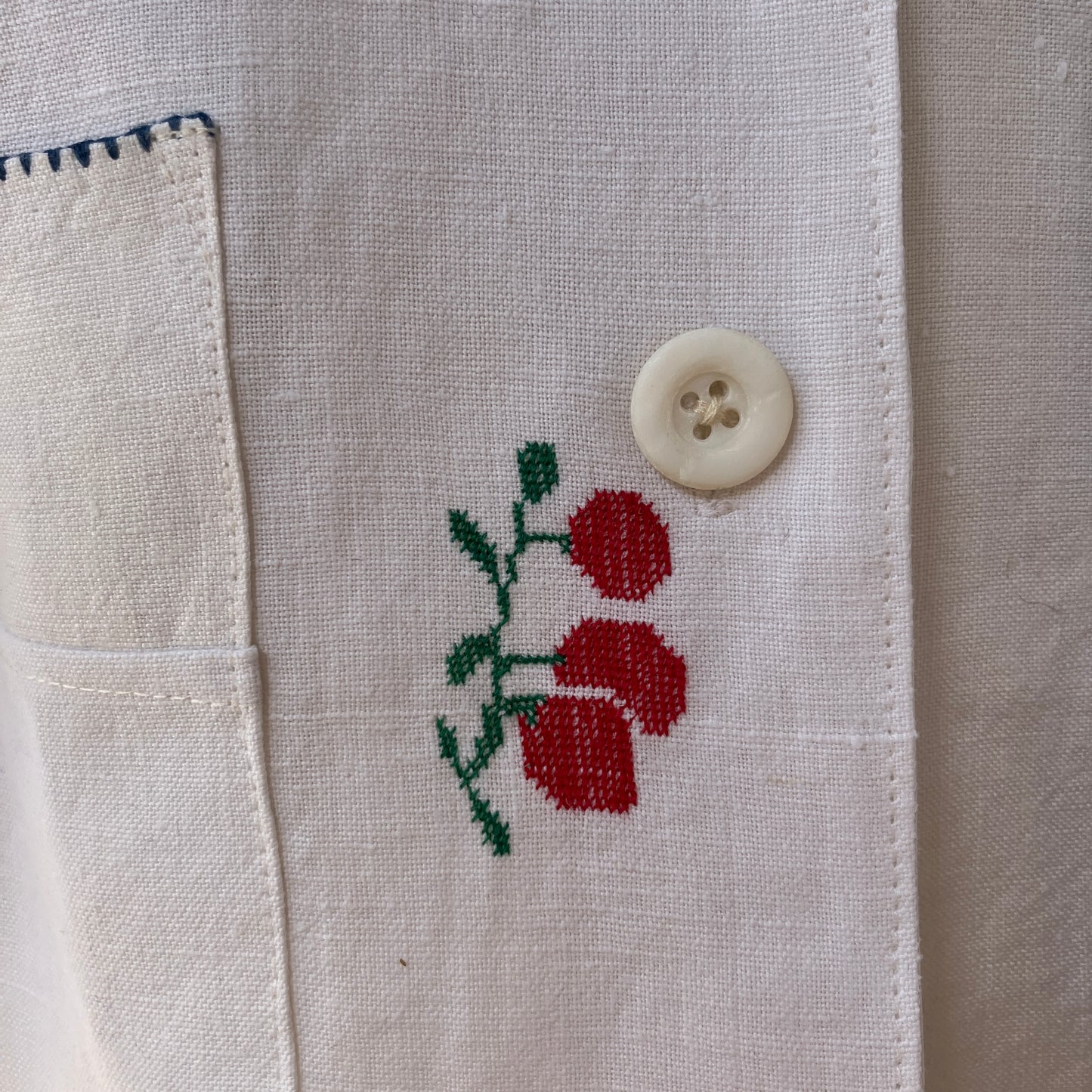 Linen shirt made from a patchwork of recycled linen tablecloths with cross-stitch motifs including dancers, flowers, trees, lemons, tomatoes and people in a horse-drawn chariot