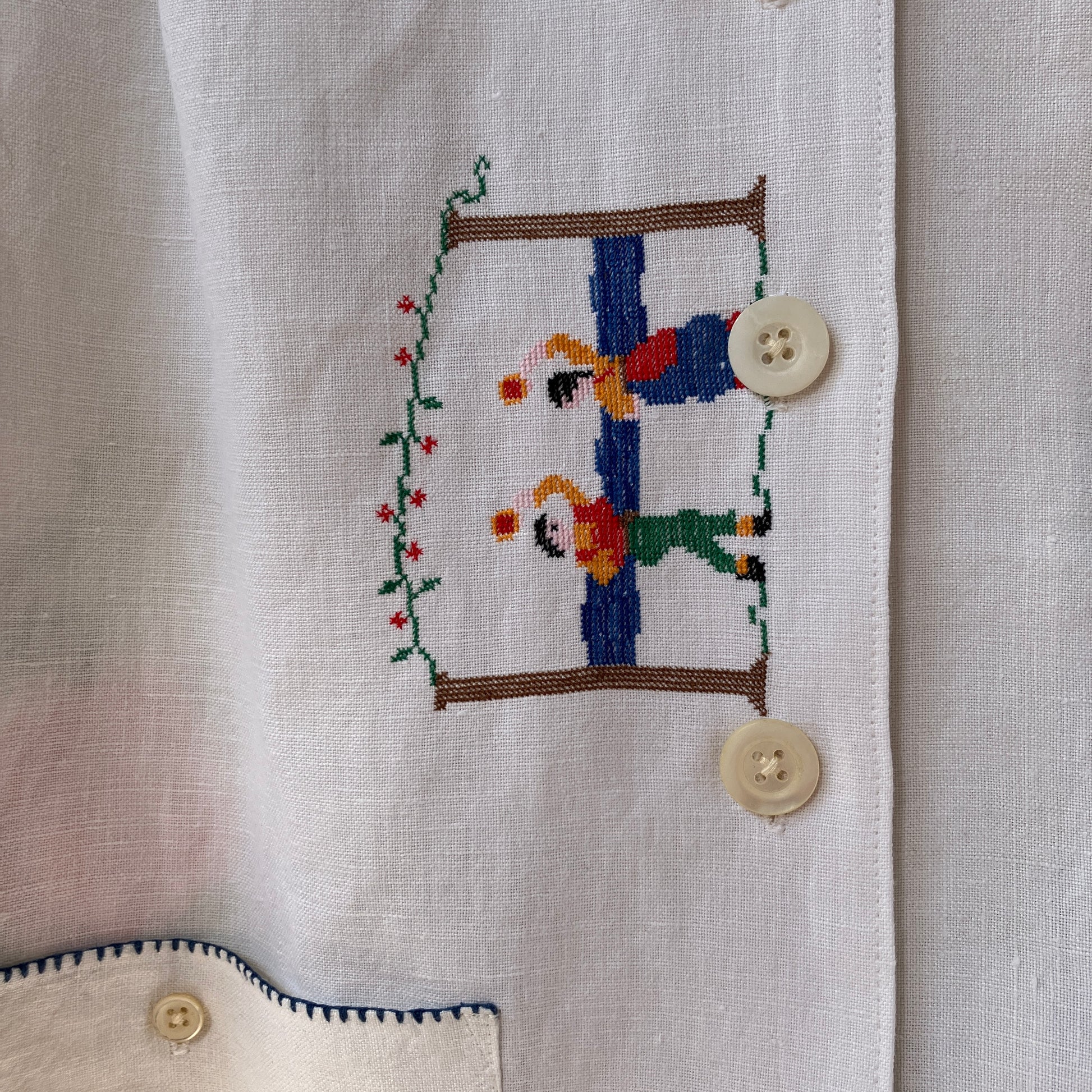 Linen shirt made from a patchwork of recycled linen tablecloths with cross-stitch motifs including dancers, flowers, trees, lemons, tomatoes and people in a horse-drawn chariot