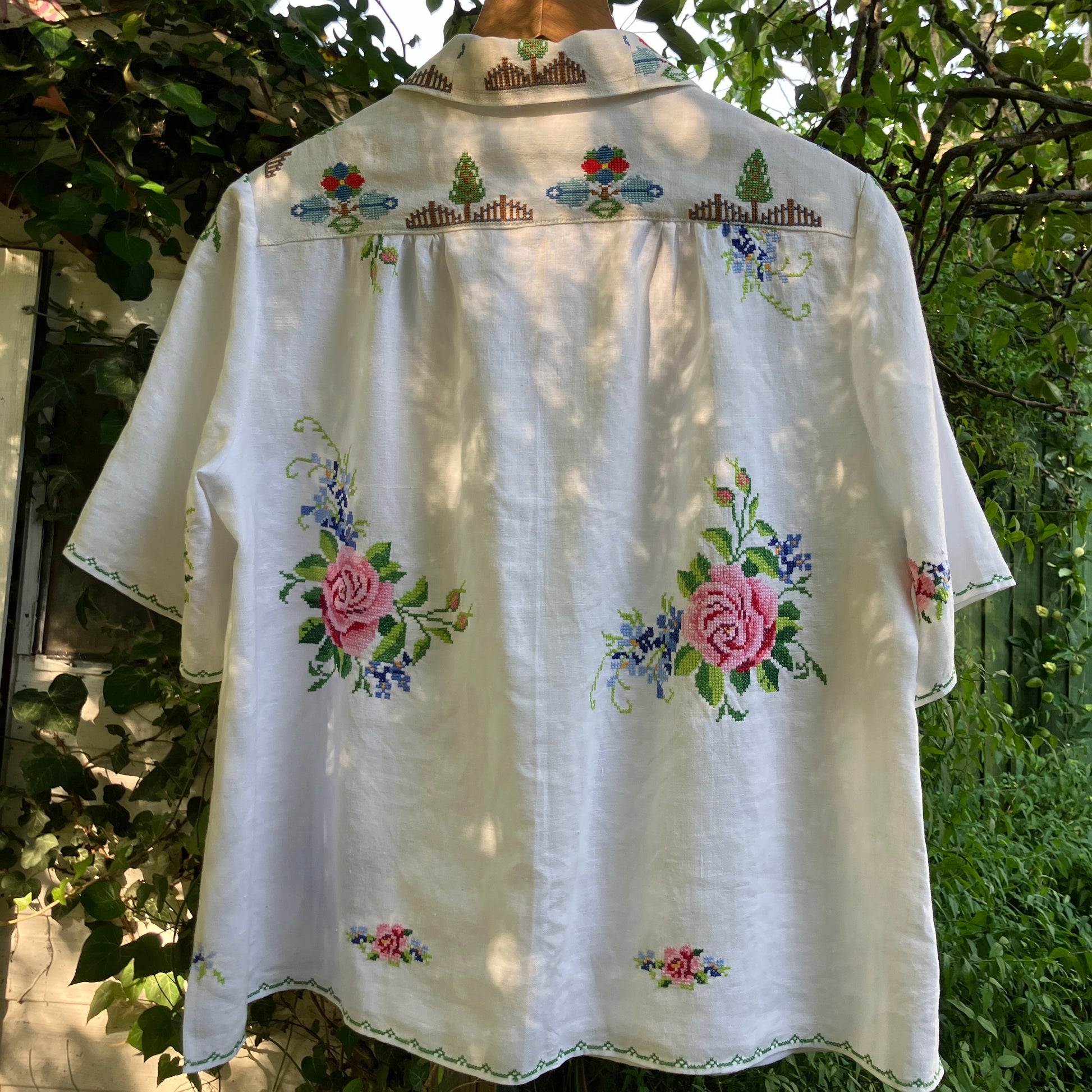 Linen shirt made from a patchwork of recycled linen tablecloths with cross-stitch motifs including dancers, flowers, trees, lemons, tomatoes and people in a horse-drawn chariot