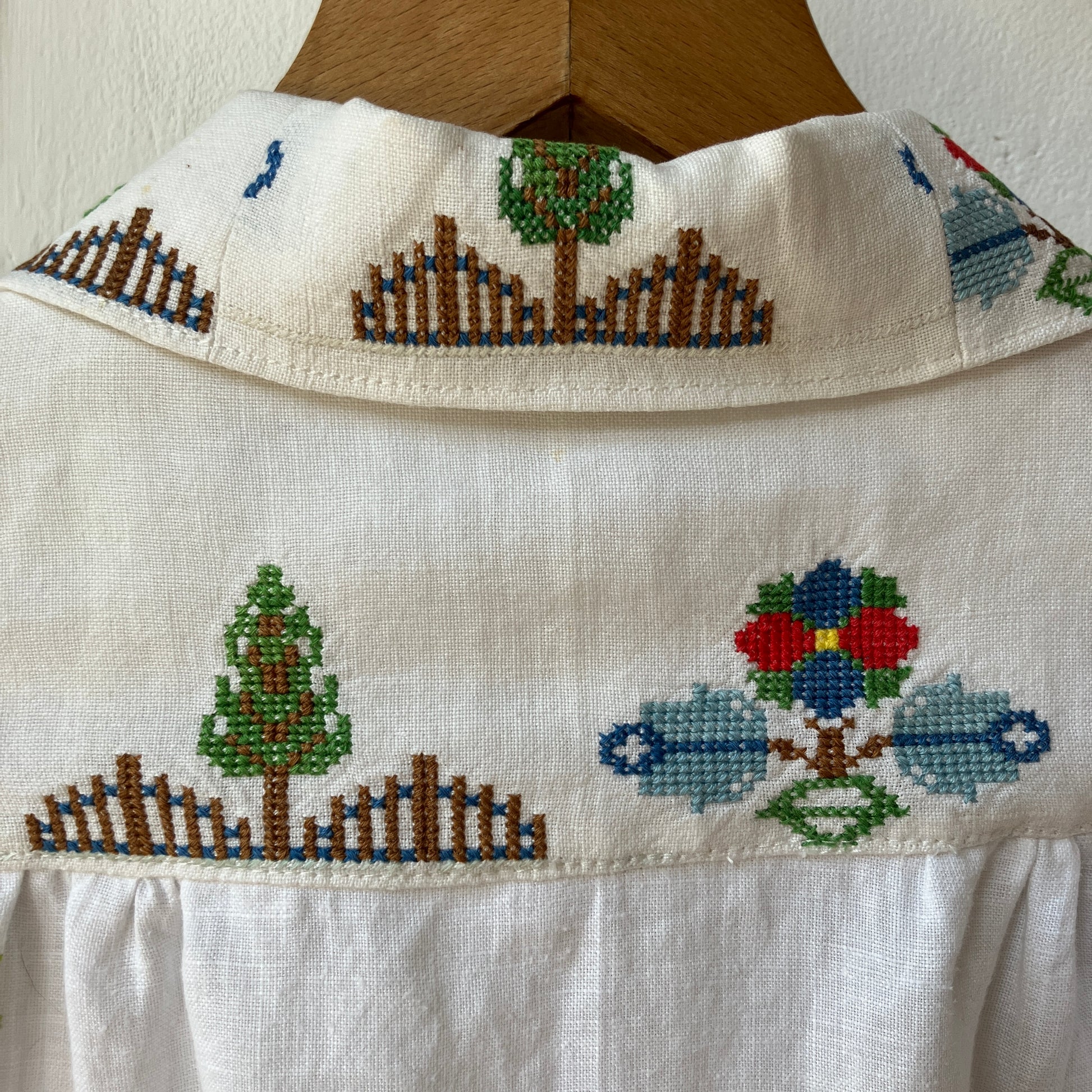 Linen shirt made from a patchwork of recycled linen tablecloths with cross-stitch motifs including dancers, flowers, trees, lemons, tomatoes and people in a horse-drawn chariot