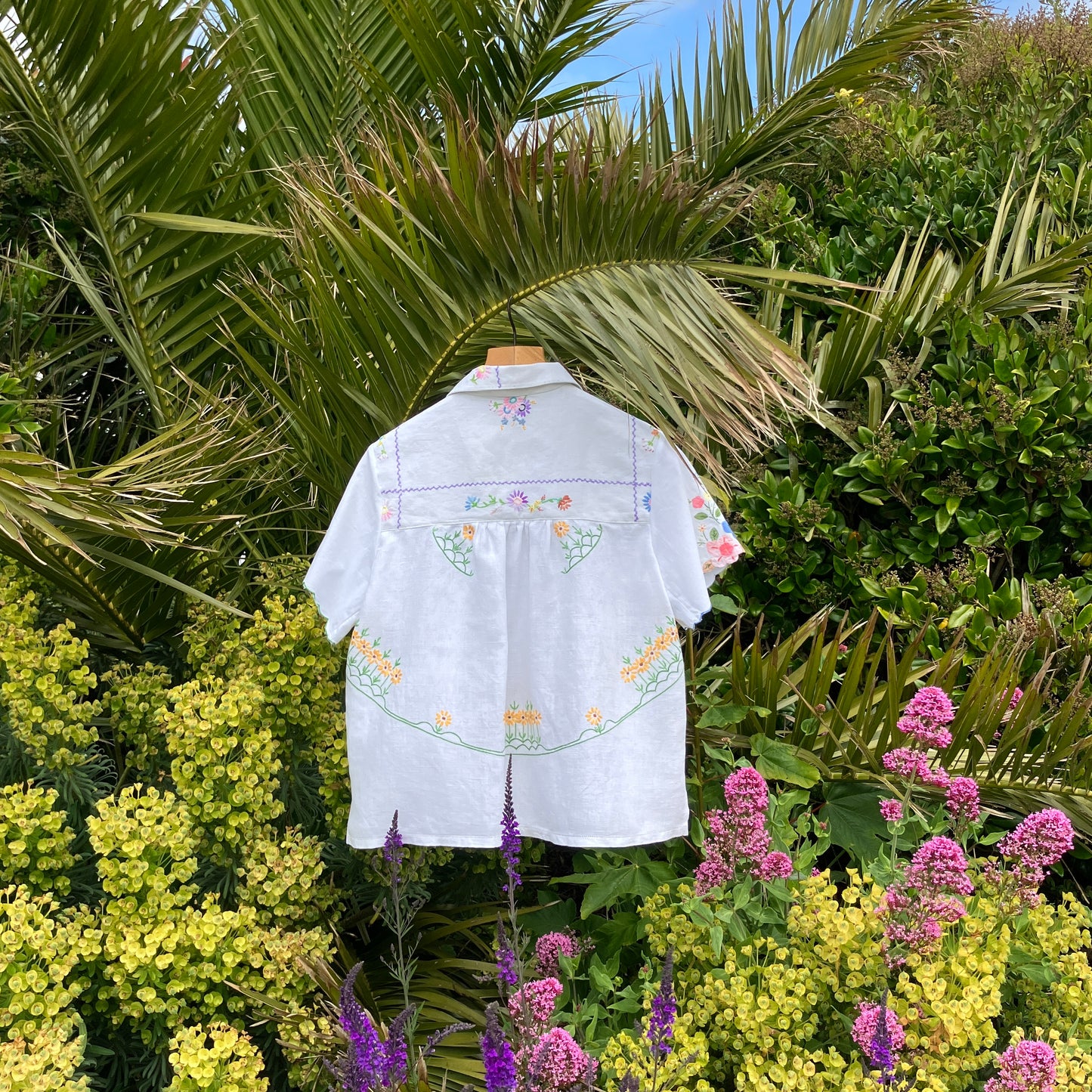 patchwork recycled tablecloth shirt hanging among some summer flowers (back view)