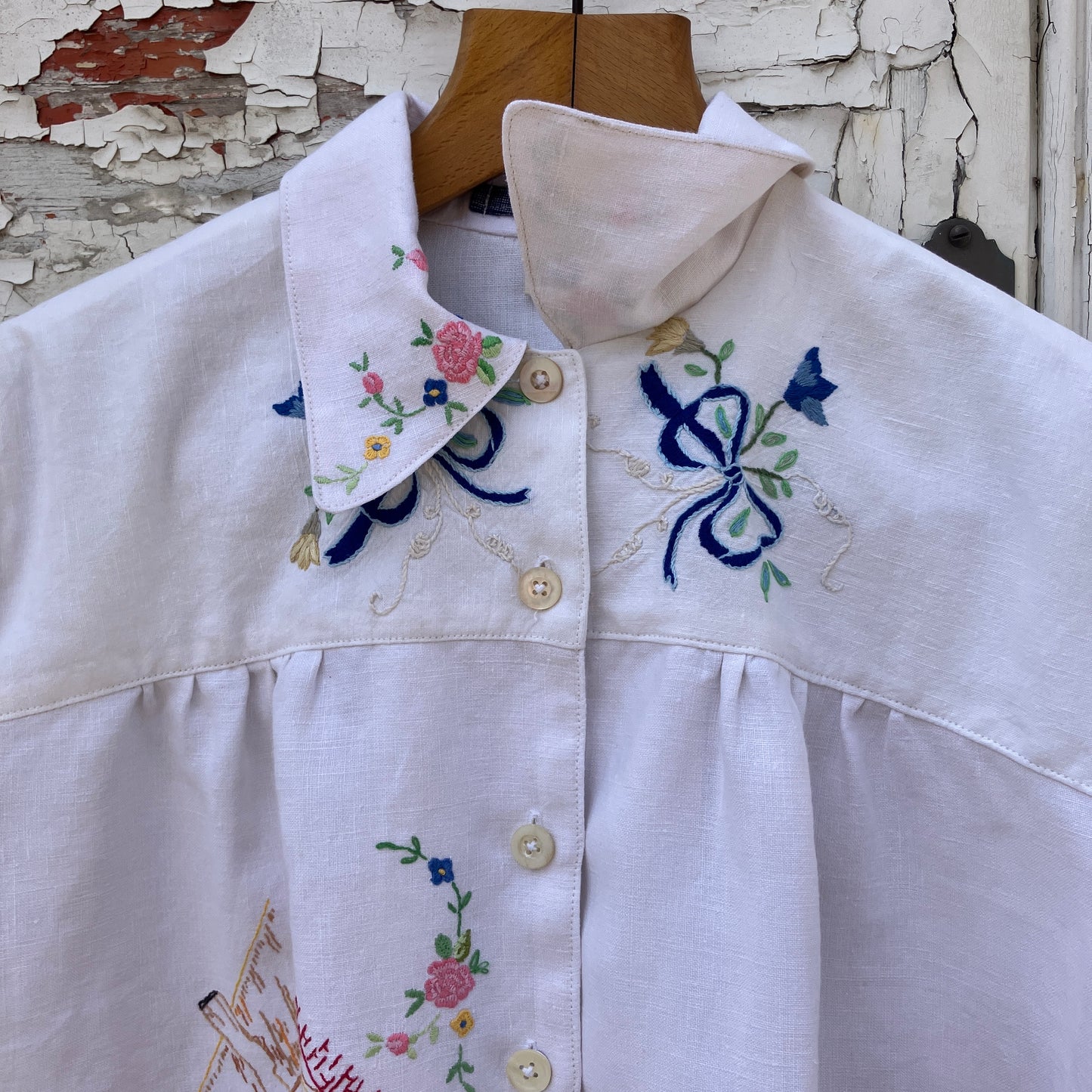 Short sleeved shirt made from a patchwork of reclaimed tablecloths with a traditional English pub with a thatched roof embroidered on the front and two bows on the yoke