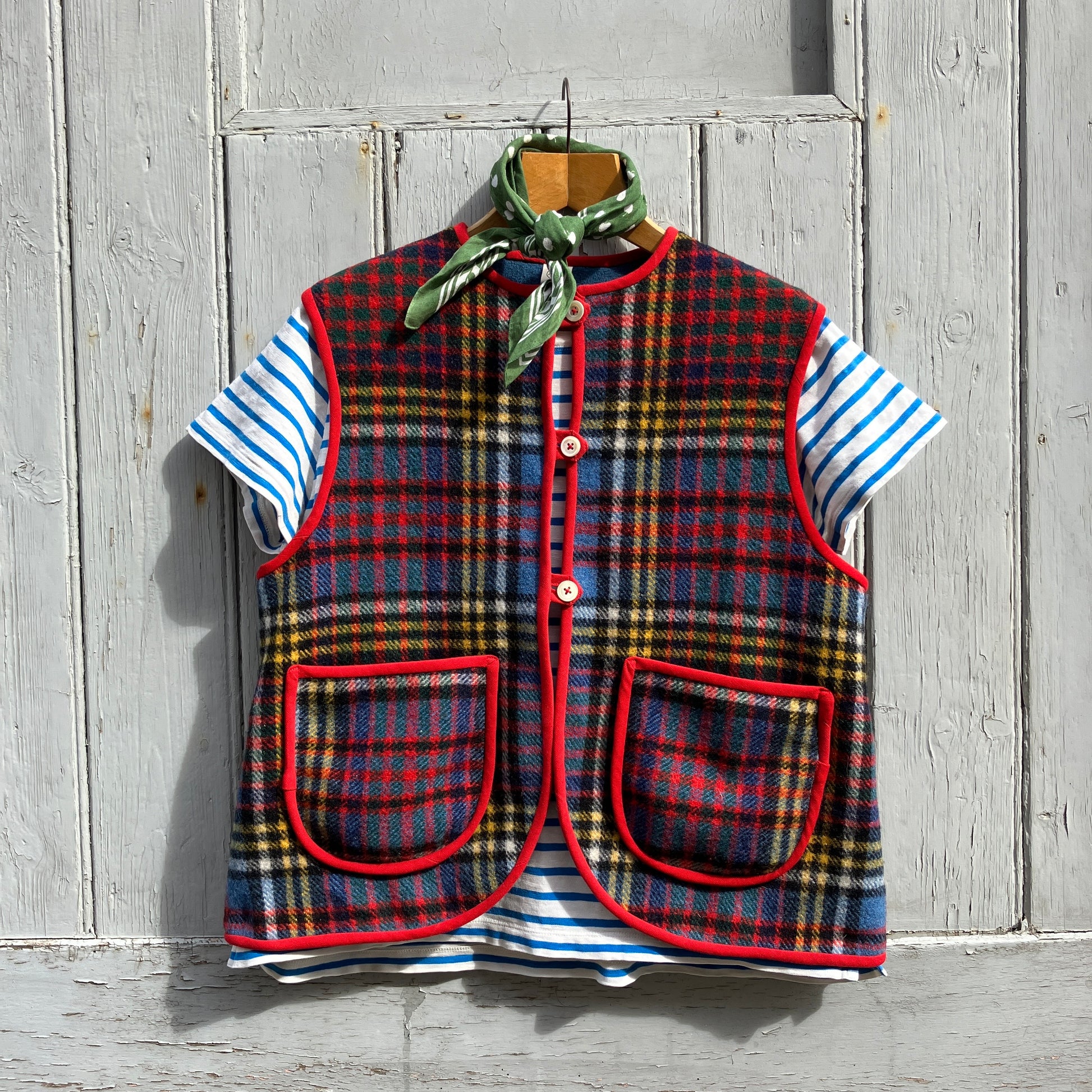 Vest/waistcoat/gilet handmade from a recycled tartan wool blanket. With red binding, two patch pockets and three shell buttons. Pictured as an outfit, with a striped T-shirt underneath