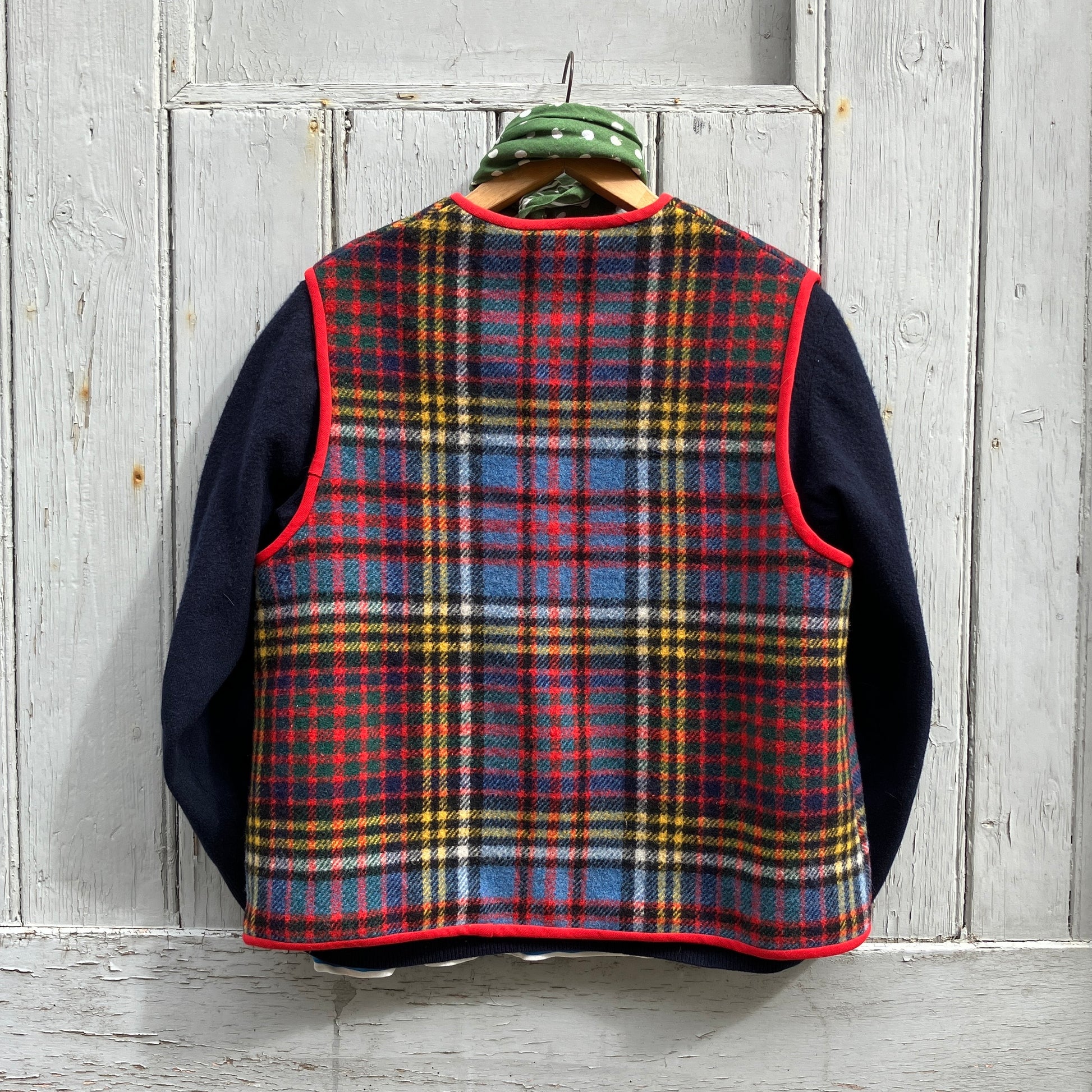 Vest/waistcoat/gilet handmade from a recycled tartan wool blanket. With red binding, two patch pockets and three shell buttons. Pictured as an outfit, with a navy jumper underneath and a green neckerchief  (back view)