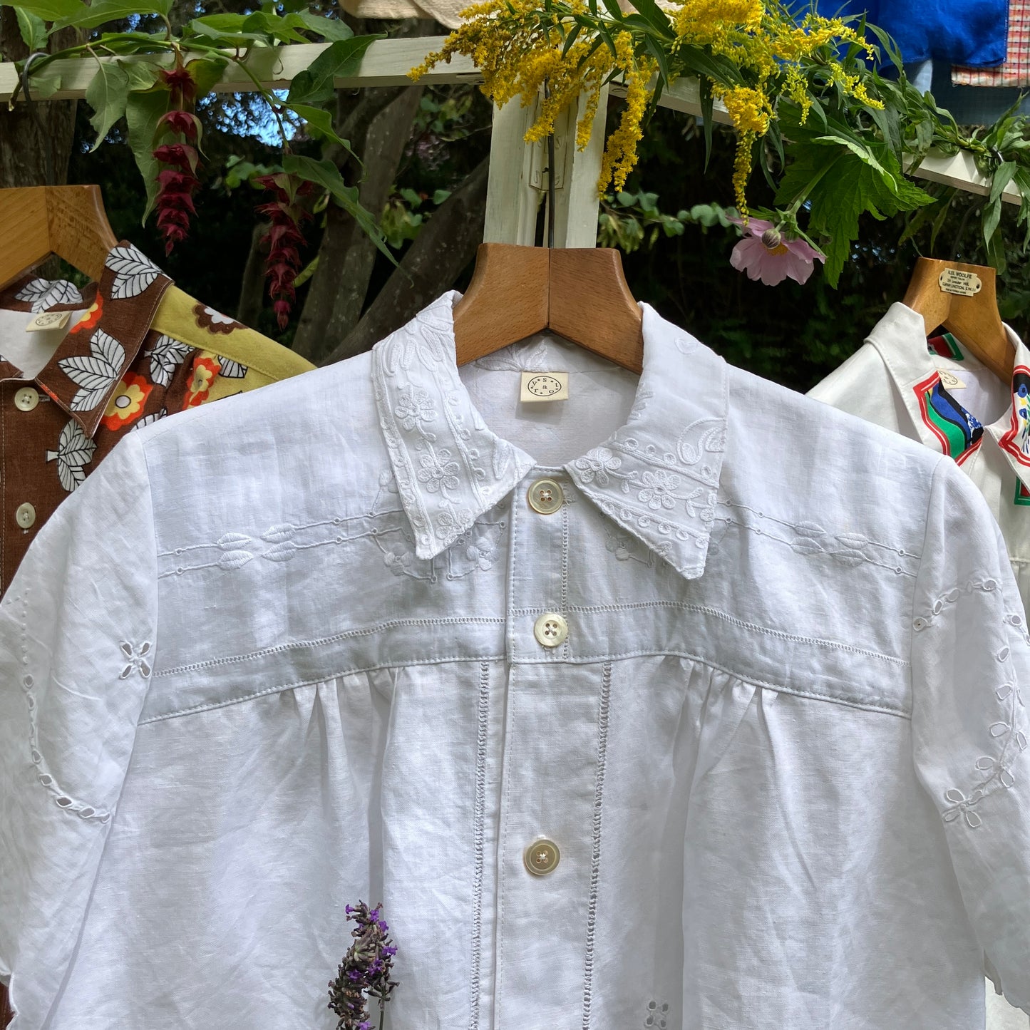 White embroidered shirt made from recycled table linen on a wooden hanger with a floral background