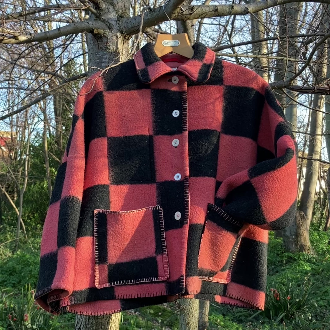 Pink and black checkerboard blanket jacket handmade from a reclaimed blanket with white buttons and blanket stitched edges. Short video of it gently moving as it hangs in a tree