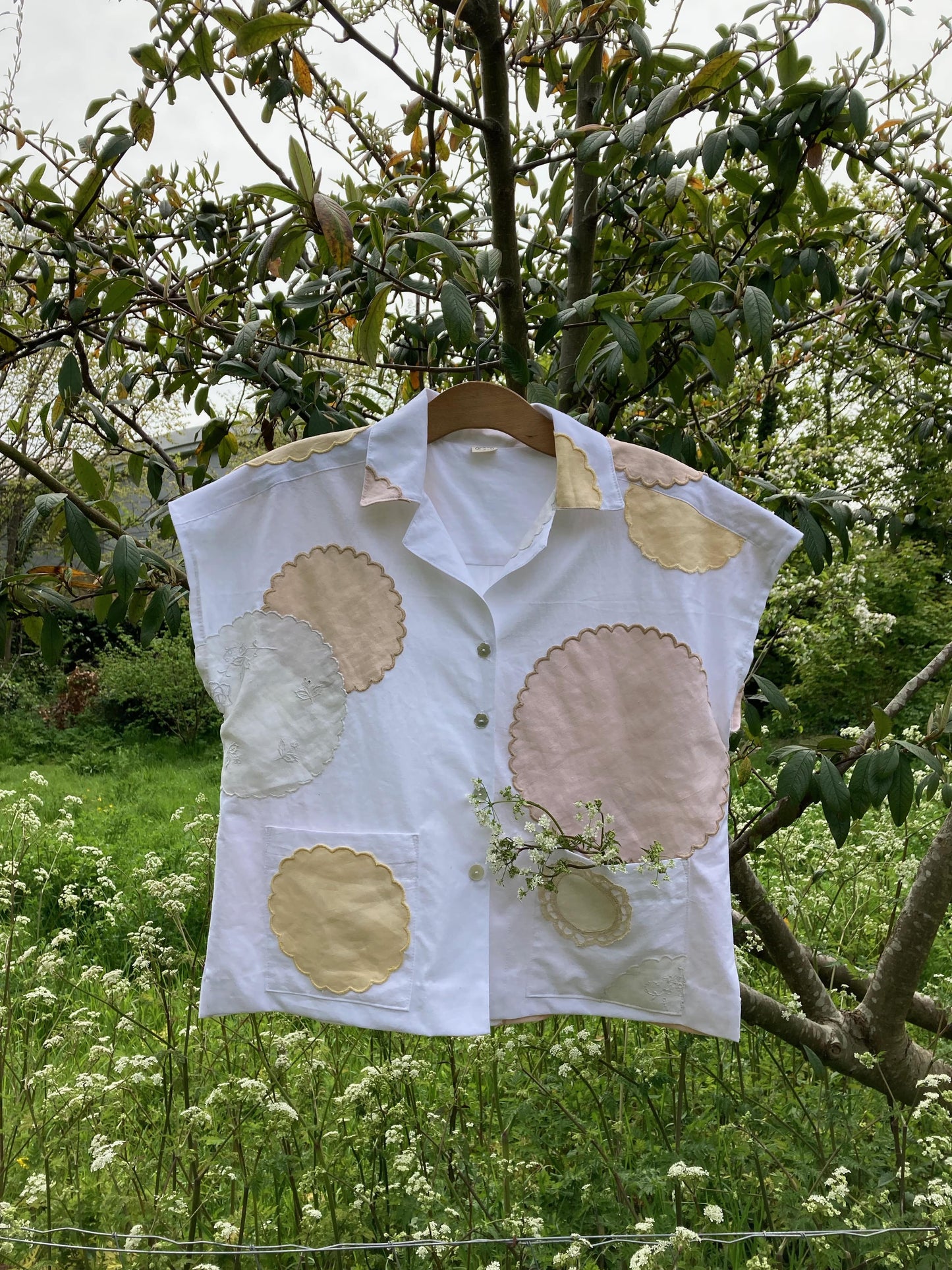 Handmade boxy shirt decorated with appliqué scallop-edge doilies shown hanging in a tree