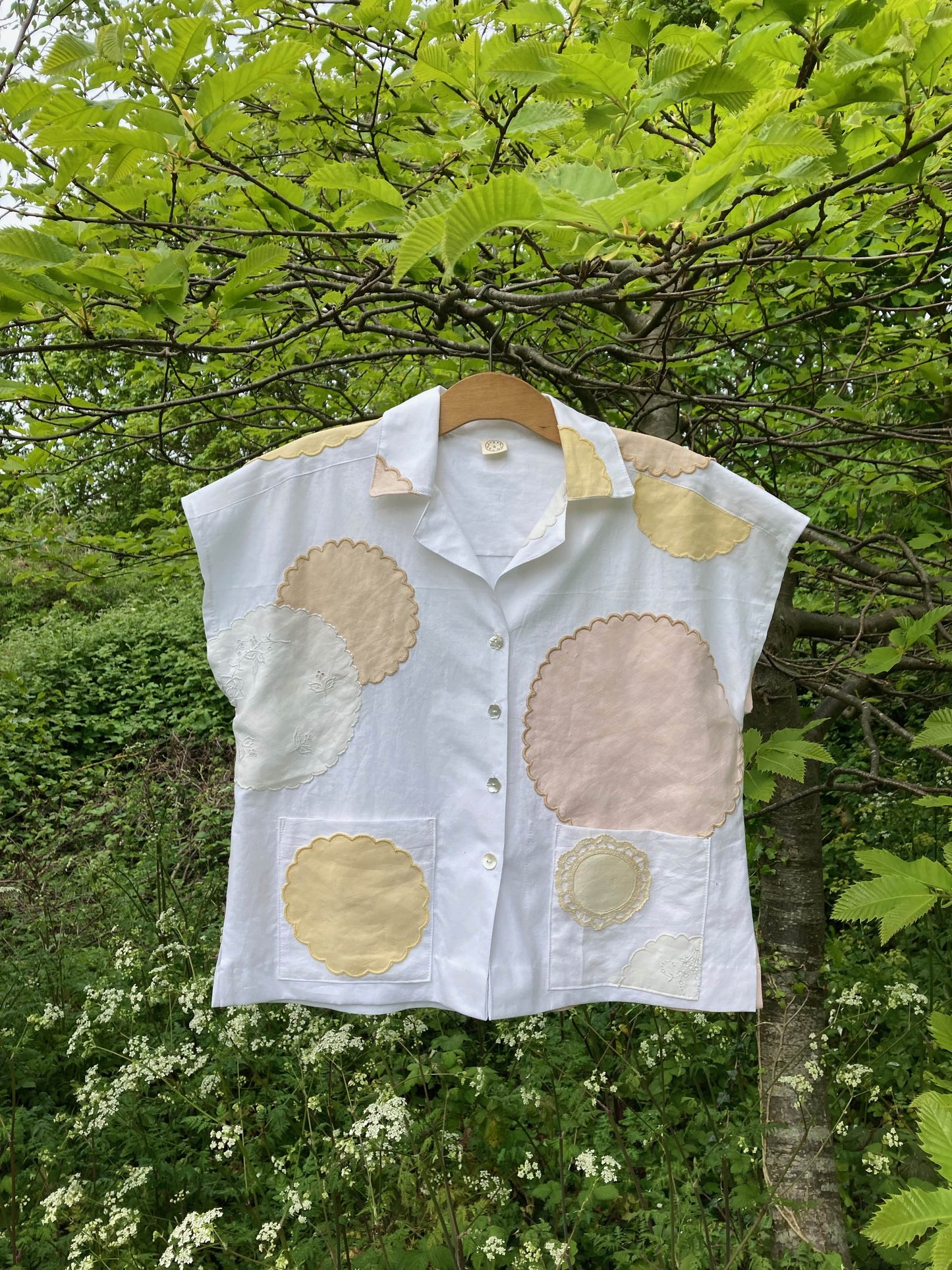 Handmade boxy shirt decorated with appliqué scallop-edge doilies shown hanging in a tree