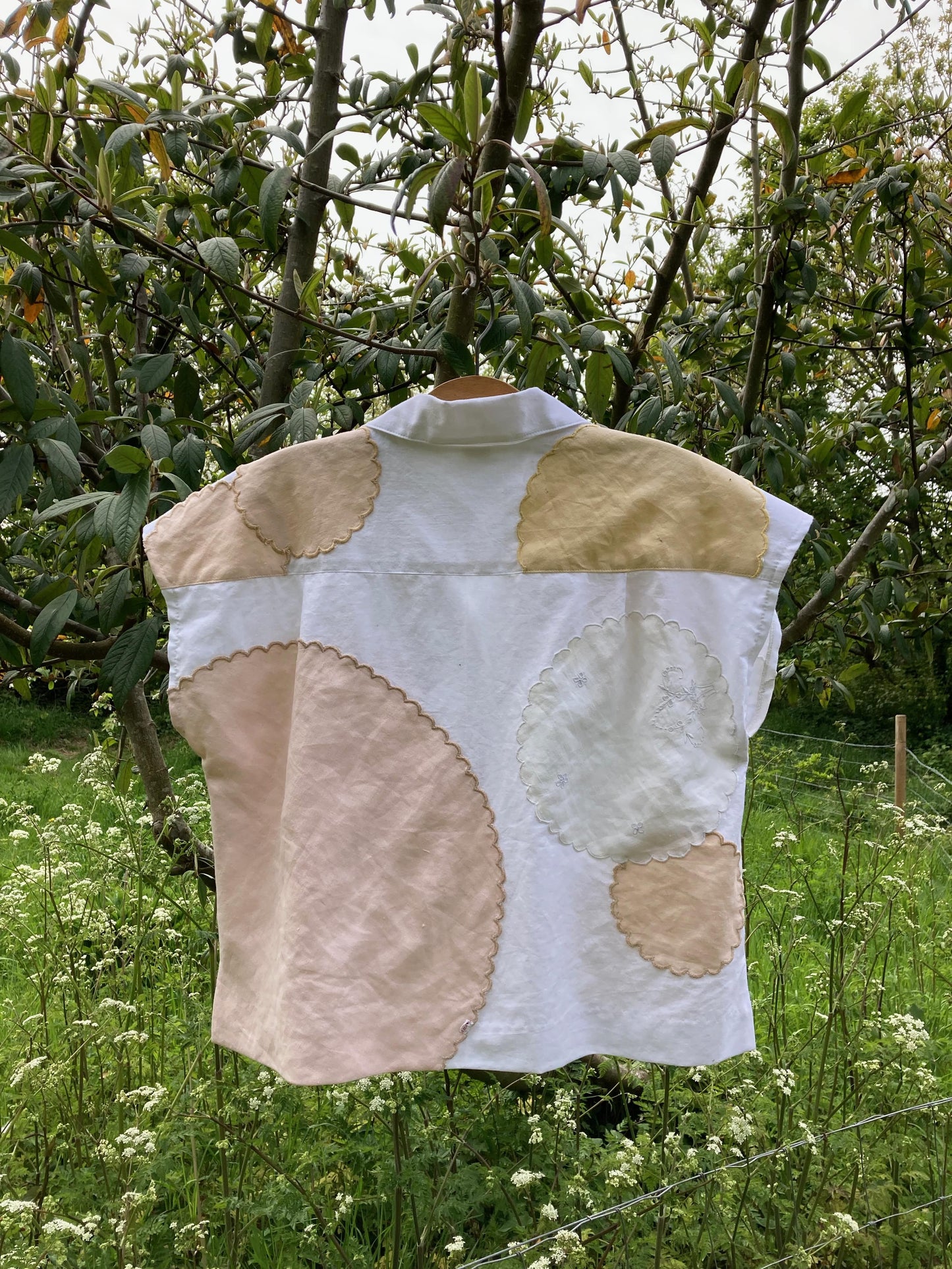 Handmade boxy shirt decorated with appliqué scallop-edge doilies shown hanging in a tree, image shows the back