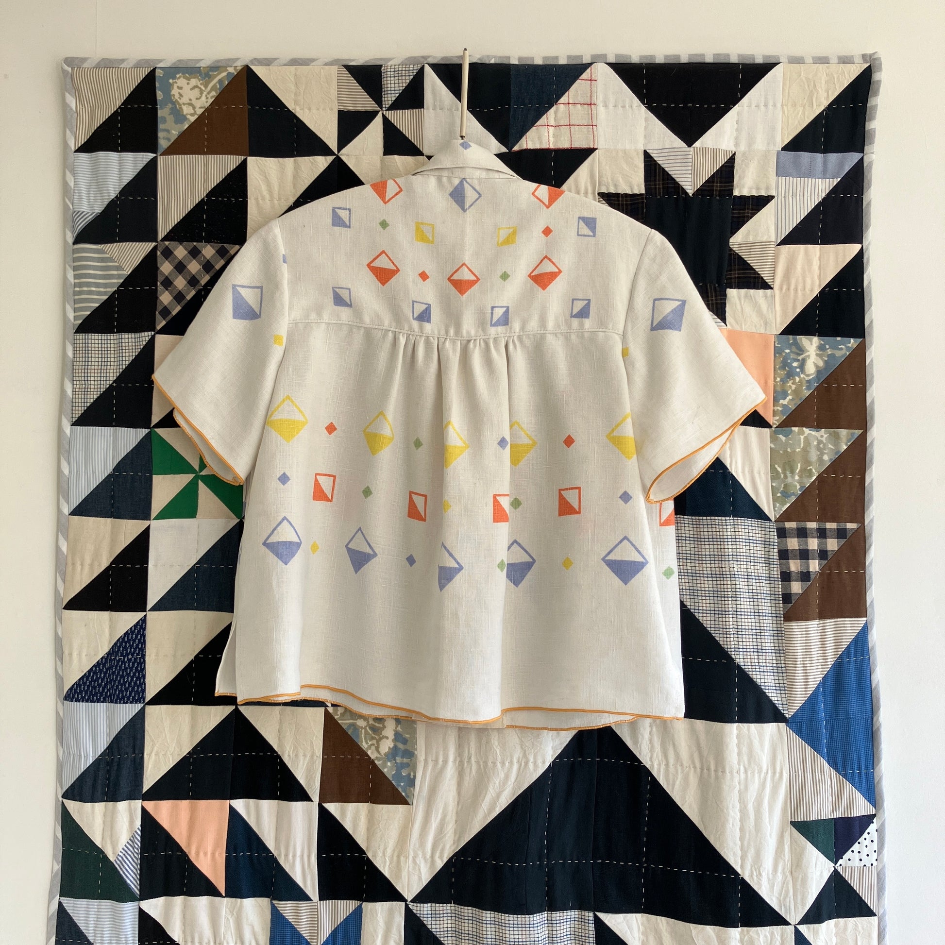 One-of-a-kind shirt handmade from a beautifully soft reclaimed off-white linen tablecloth with a cool geometric print. Photographed against a patchwork quilt