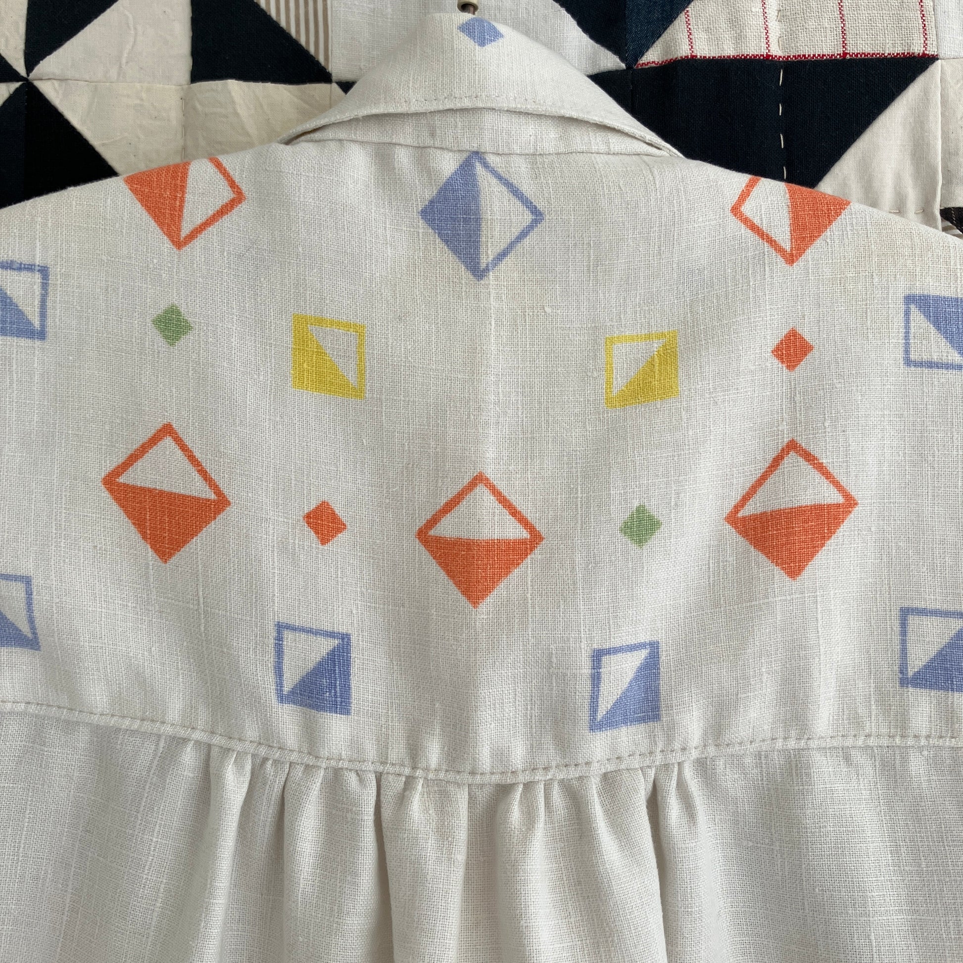 One-of-a-kind shirt handmade from a beautifully soft reclaimed off-white linen tablecloth with a cool geometric print. Photographed against a patchwork quilt (close-up of back)