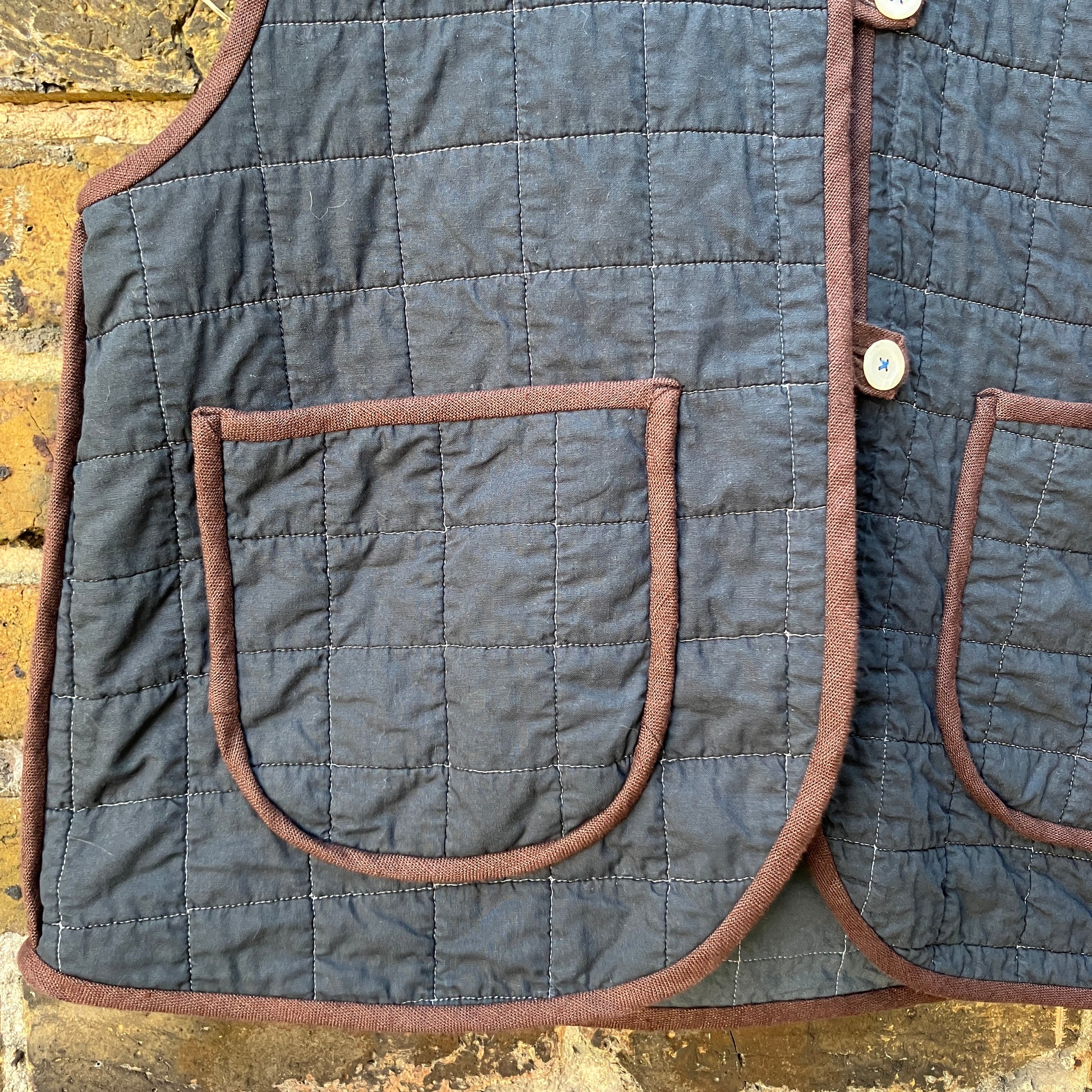 Super useful vest/gilet/bodywarmer/waistcoat handmade from a reclaimed black cotton quilt. Features two large patch pockets, three found shell buttons and brown linen binding.