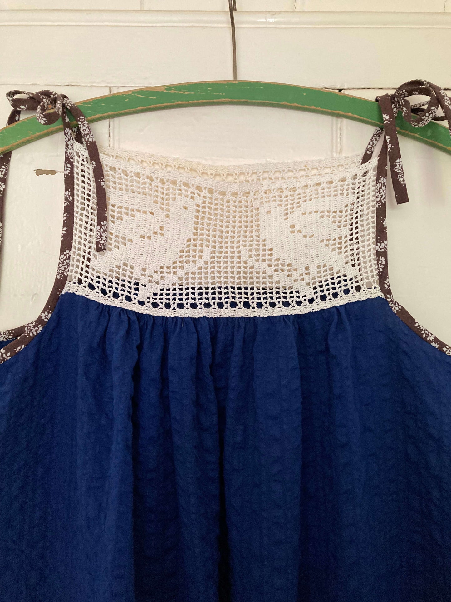 Close-up of hand stitched blue and white light and airy summer dress made from recycled cotton seersucker with a vintage bird-motif crochet yoke, tie straps and two patch pockets
