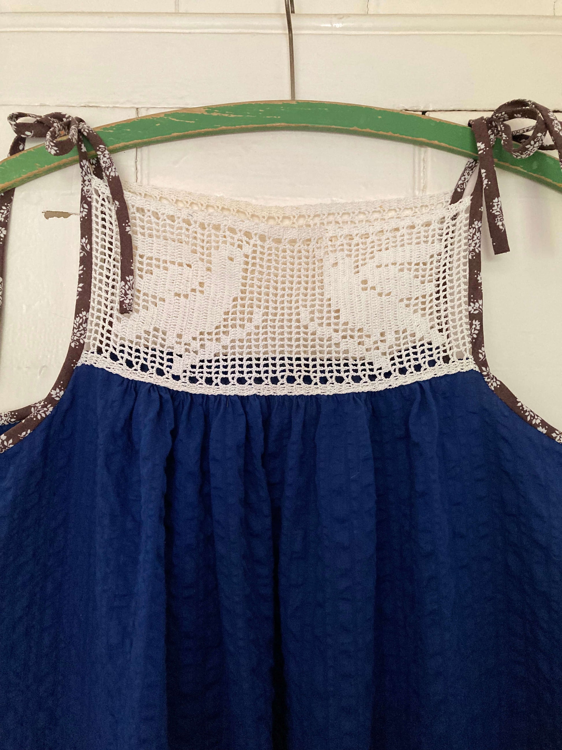 Close-up of hand stitched blue and white light and airy summer dress made from recycled cotton seersucker with a vintage bird-motif crochet yoke, tie straps and two patch pockets