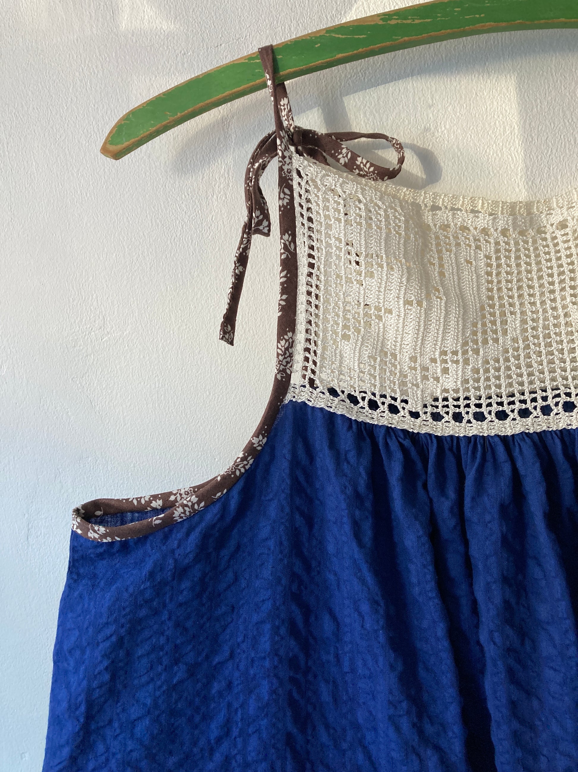 Close-up of hand stitched blue and white light and airy summer dress made from recycled cotton seersucker with a vintage bird-motif crochet yoke, tie straps and two patch pockets