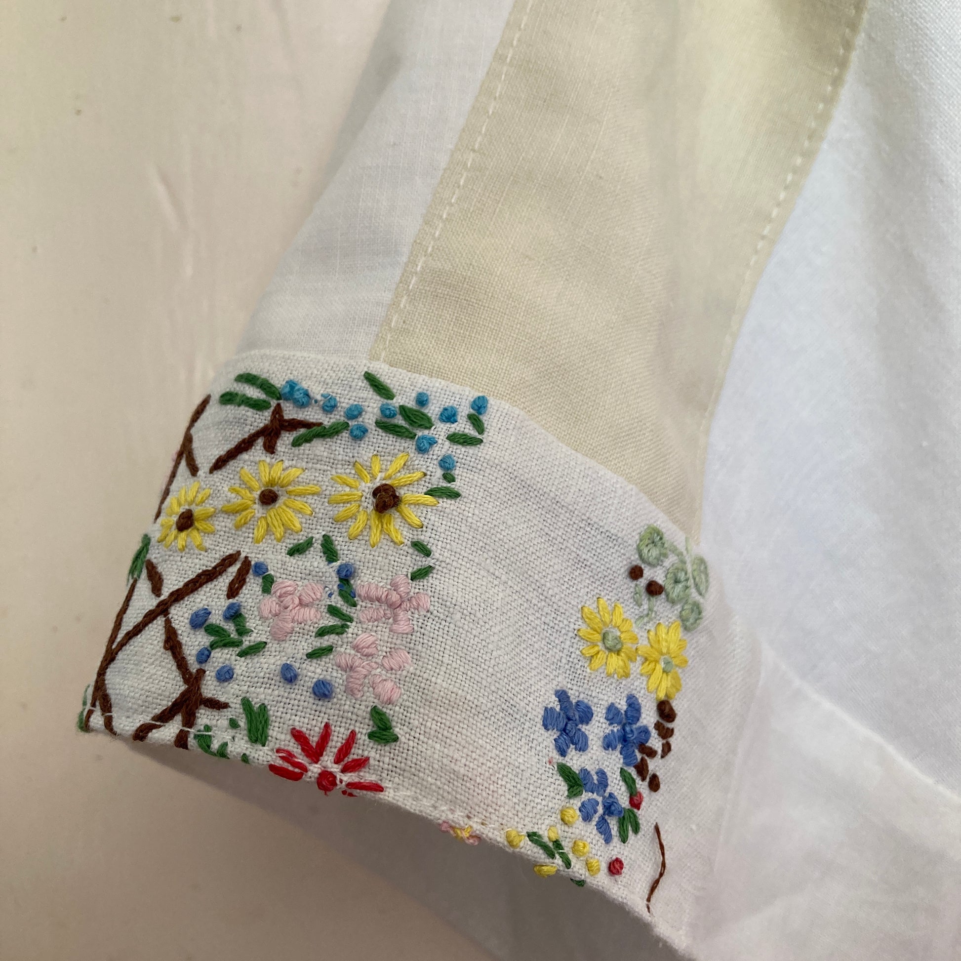 Short-sleeved boxy top made from vintage embroidered linen tablecloths. Mostly white and off-white with wide pink stripes and embroidered details include cherries and flowers (sleeve detail)