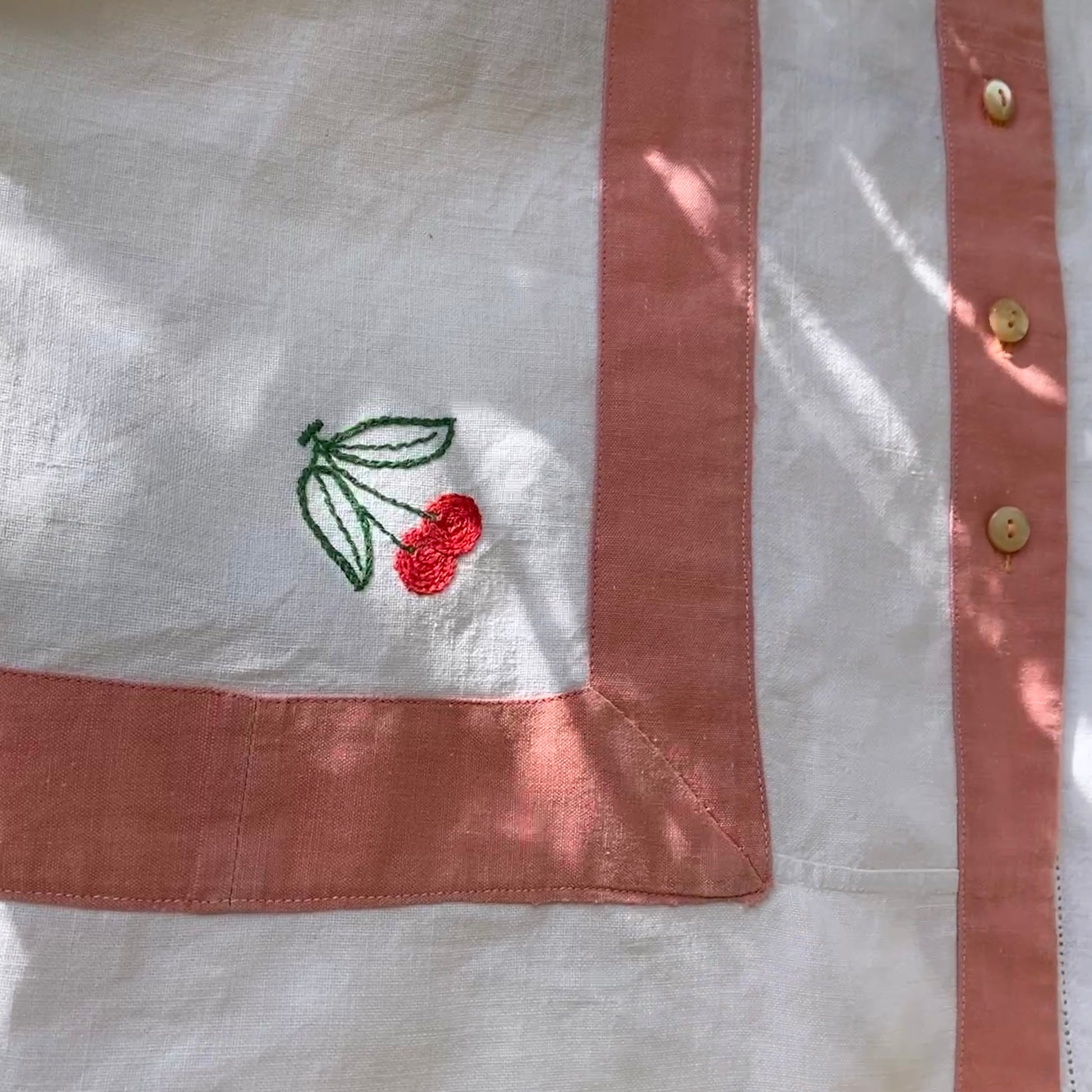 Short-sleeved boxy top made from vintage embroidered linen tablecloths. Mostly white and off-white with wide pink stripes and embroidered details include cherries and flowers (cherry detail)