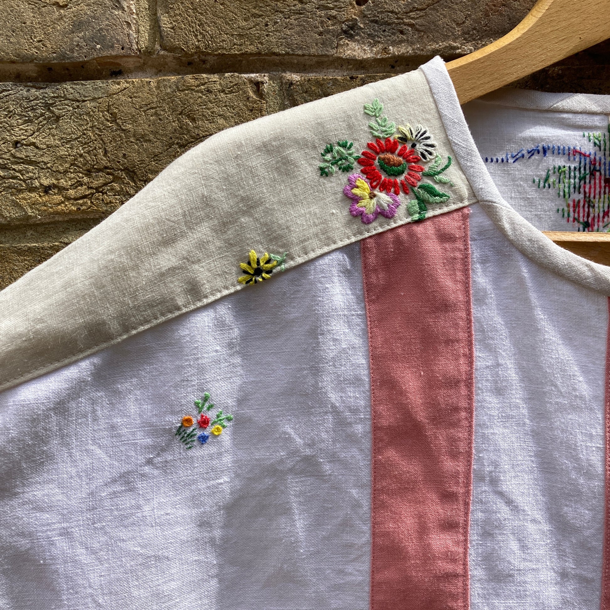 Short-sleeved boxy top made from vintage embroidered linen tablecloths. Mostly white and off-white with wide pink stripes and embroidered details include cherries and flowers (shoulder detail)