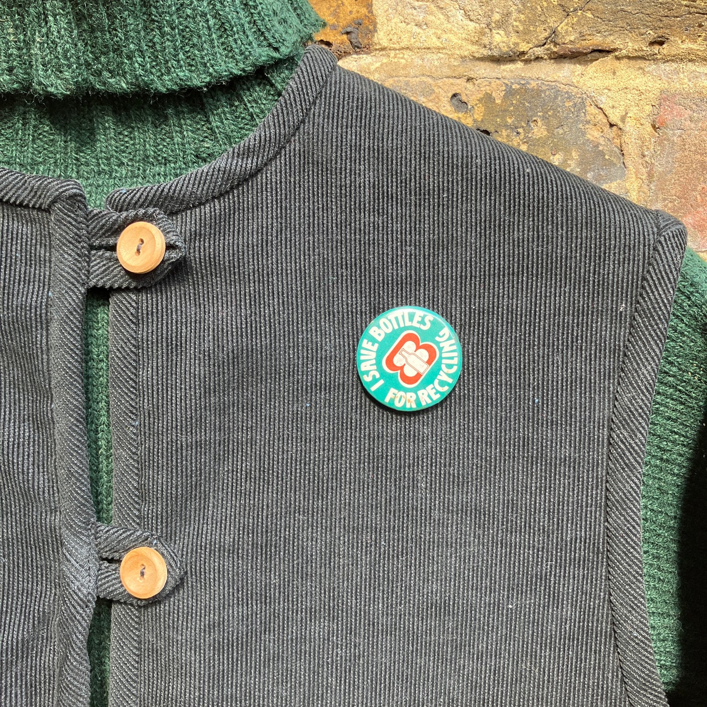 Needlecord vest/gilet/waistcoat with large hand quilted patchwork pockets in gold and silver lamé with blue binding. Finished with wooden buttons and a hanging loop. Pictured hanging against a wall with a vintage badge pinned to it that reads 'I save bottles for recycling'