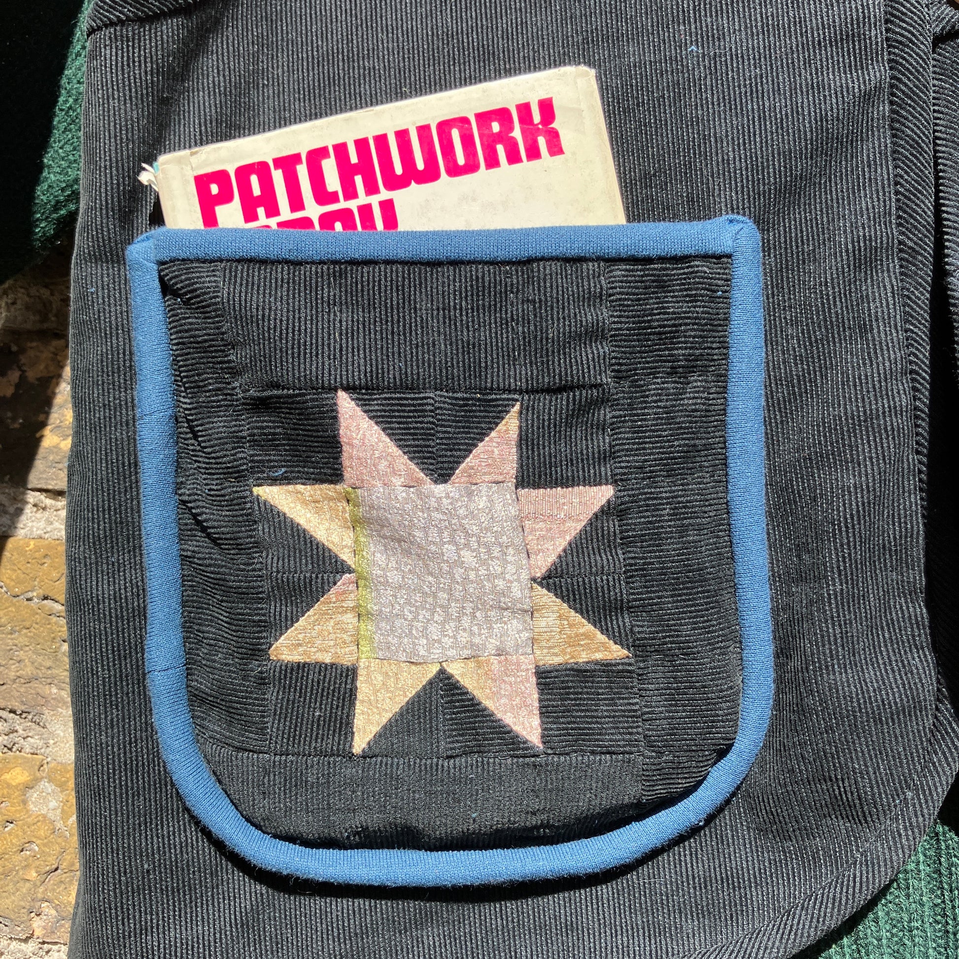 Needlecord vest/gilet/waistcoat with large hand quilted patchwork pockets in gold and silver lamé with blue binding.  Finished with wooden buttons and a hanging loop. Close-up of one of the pockets with a vintage patchwork book sticking out