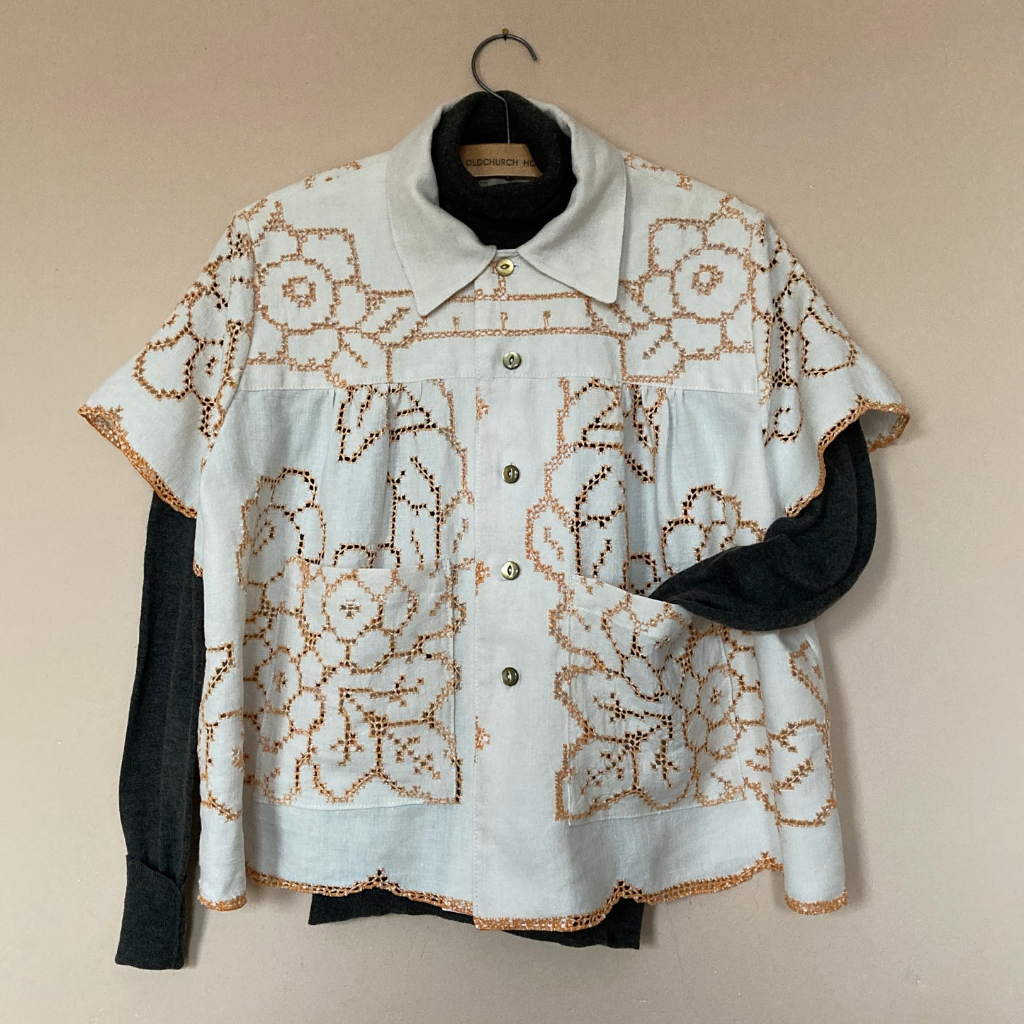 Short-sleeved shirt made from a recycled off-white linen tablecloth with orange cutwork pattern. Shown with a dark cloloured base layer underneath