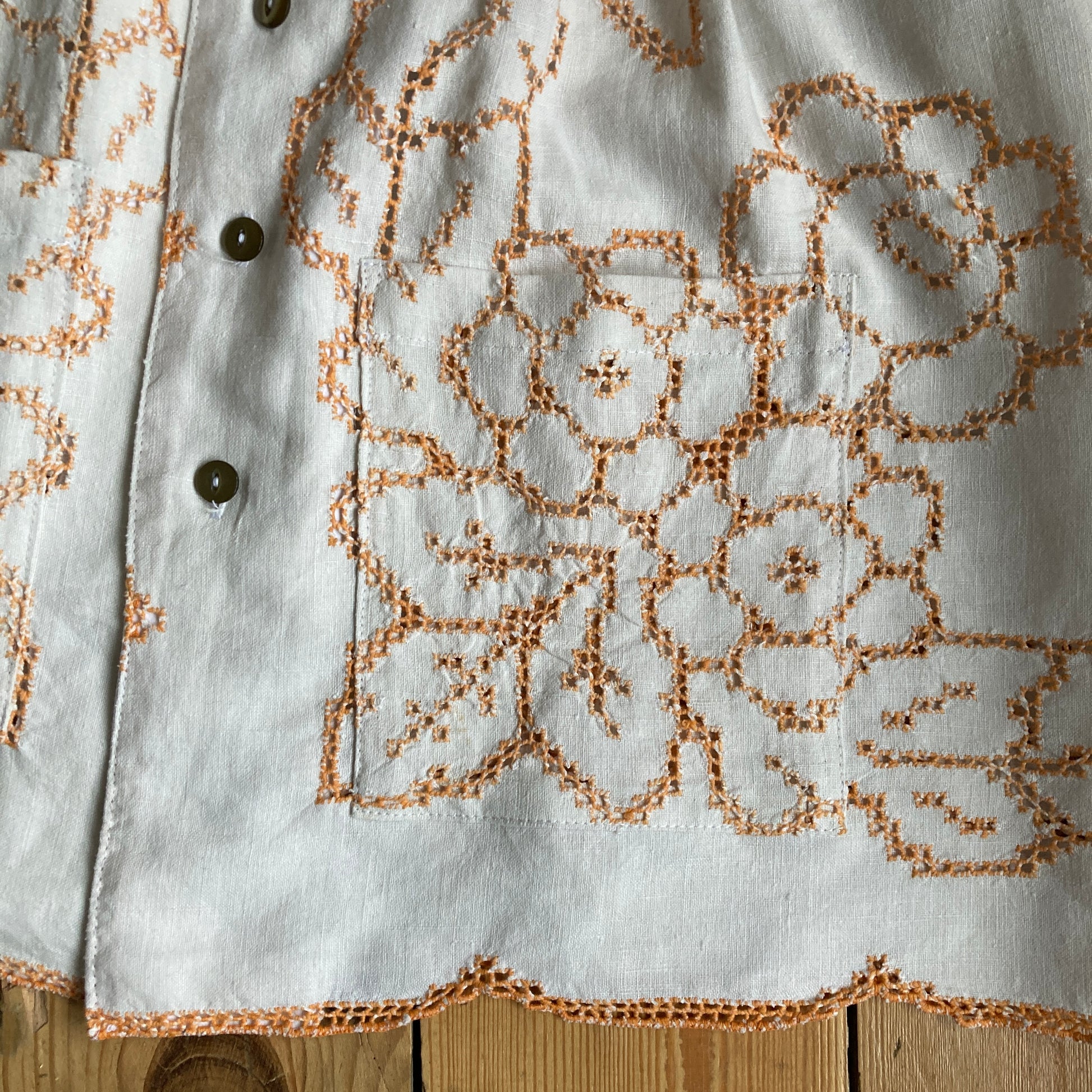 Short-sleeved shirt made from a recycled off-white linen tablecloth with orange cutwork pattern (detail of pocket)