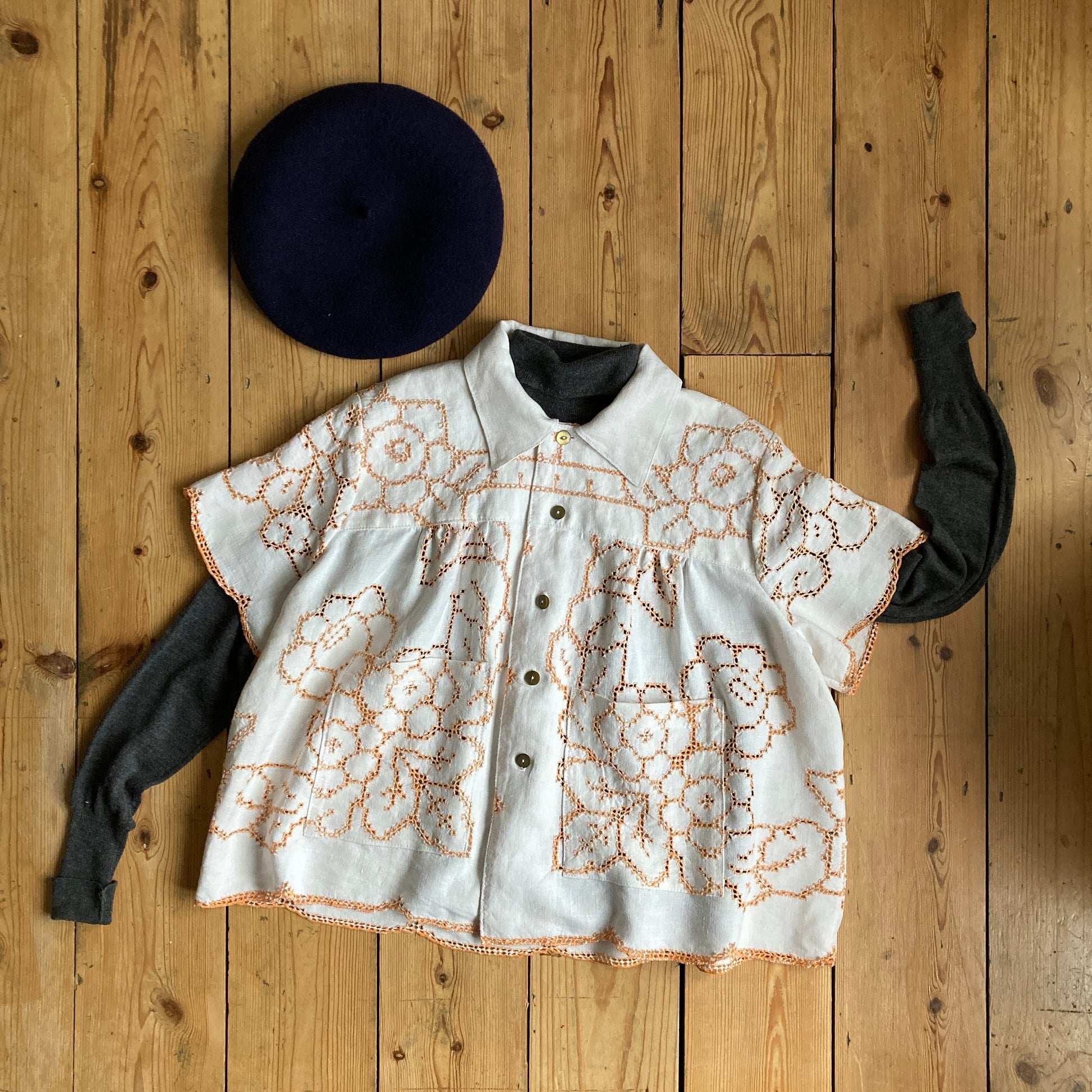 Short-sleeved shirt made from a recycled off-white linen tablecloth with orange cutwork pattern (flat lay version)