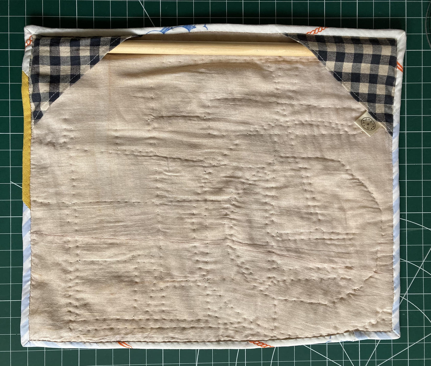 Wallhanging made from precious neutral and brightly-coloured scraps patchworked together and quilted in an improv fashion, image shows the back