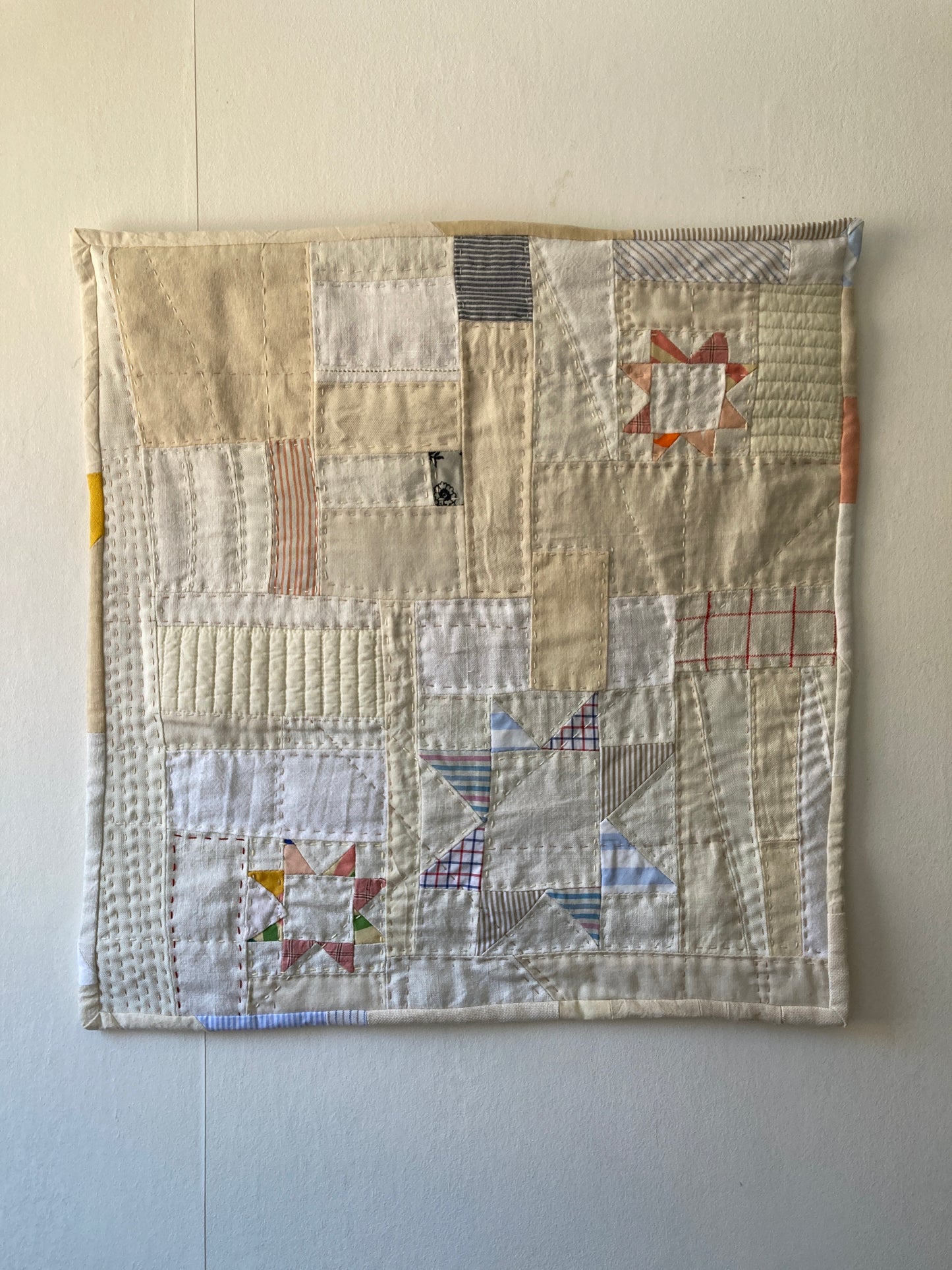 Wallhanging made from precious neutral and pastel-coloured scraps patchworked together and quilted in an improv fashion